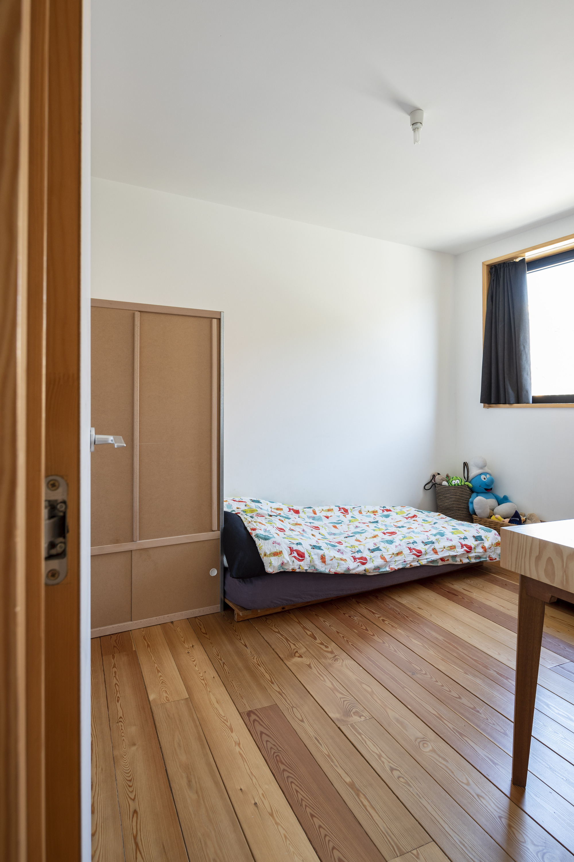 Bedroom with timber flooring, built-in wardrobe and window with dark curtain in natural light