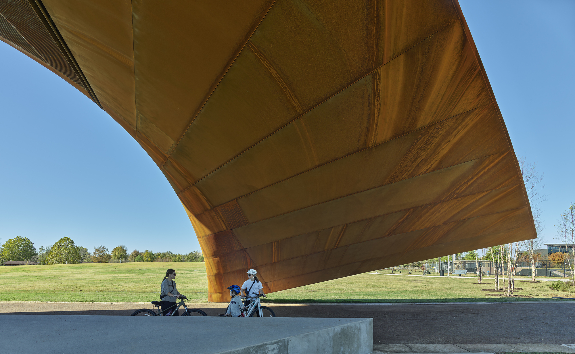 Two people seated on a concrete bench beneath the sloping wood canopy edge