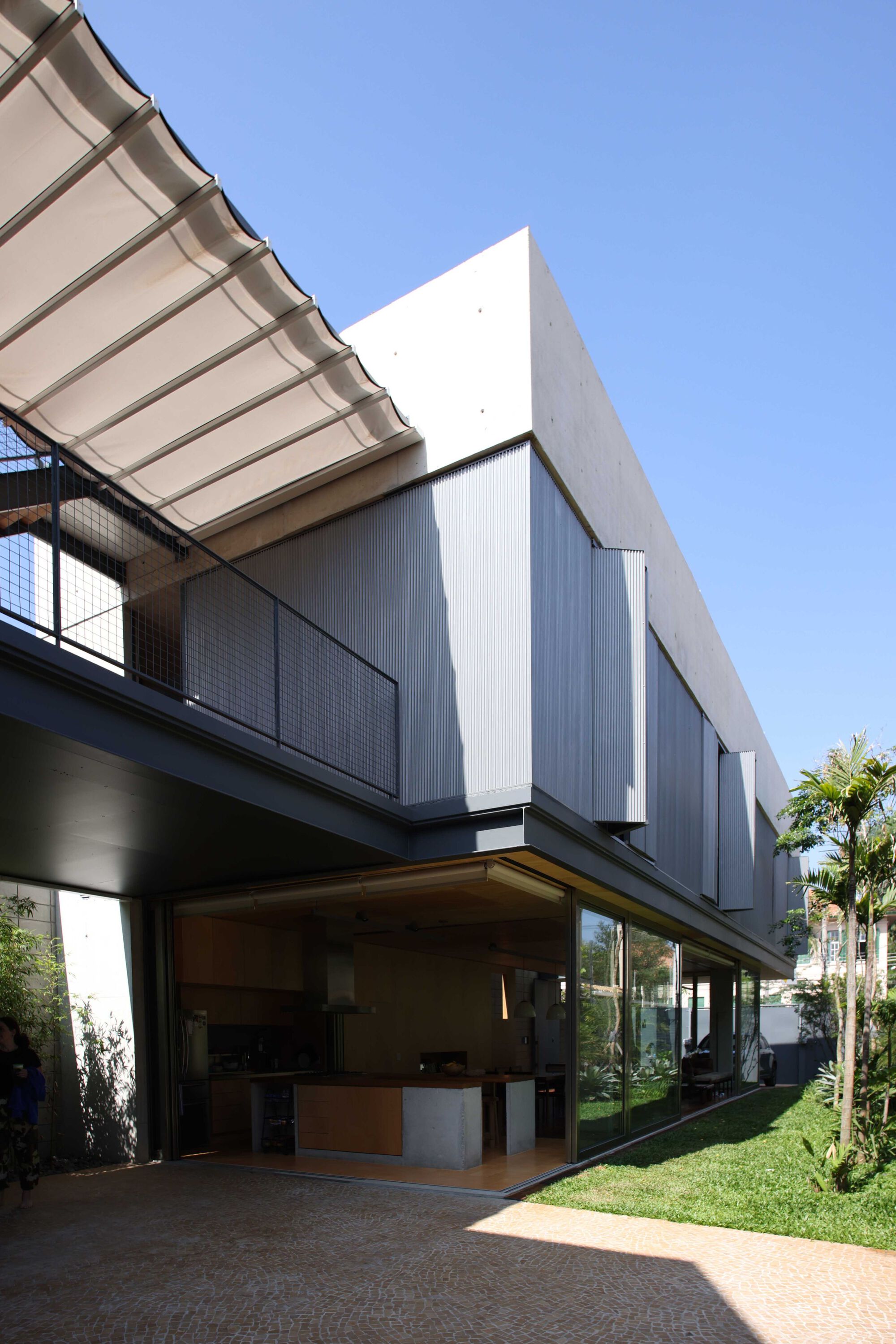 Cantilevered upper volume with corrugated metal cladding and retractable awning over open ground floor