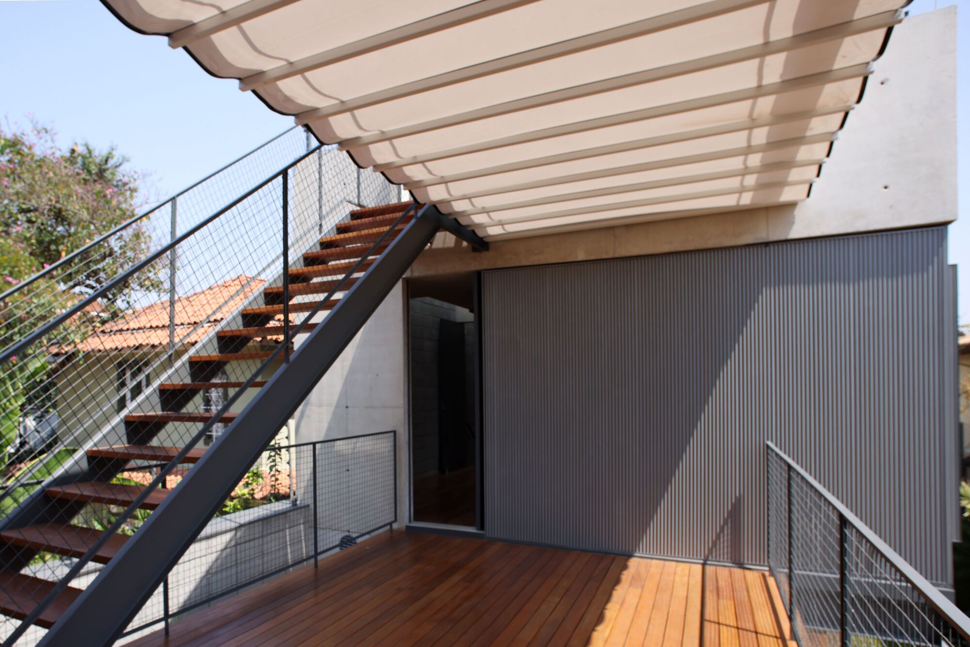 View of the slatted timber canopy overhead and corrugated metal wall beside the wooden deck