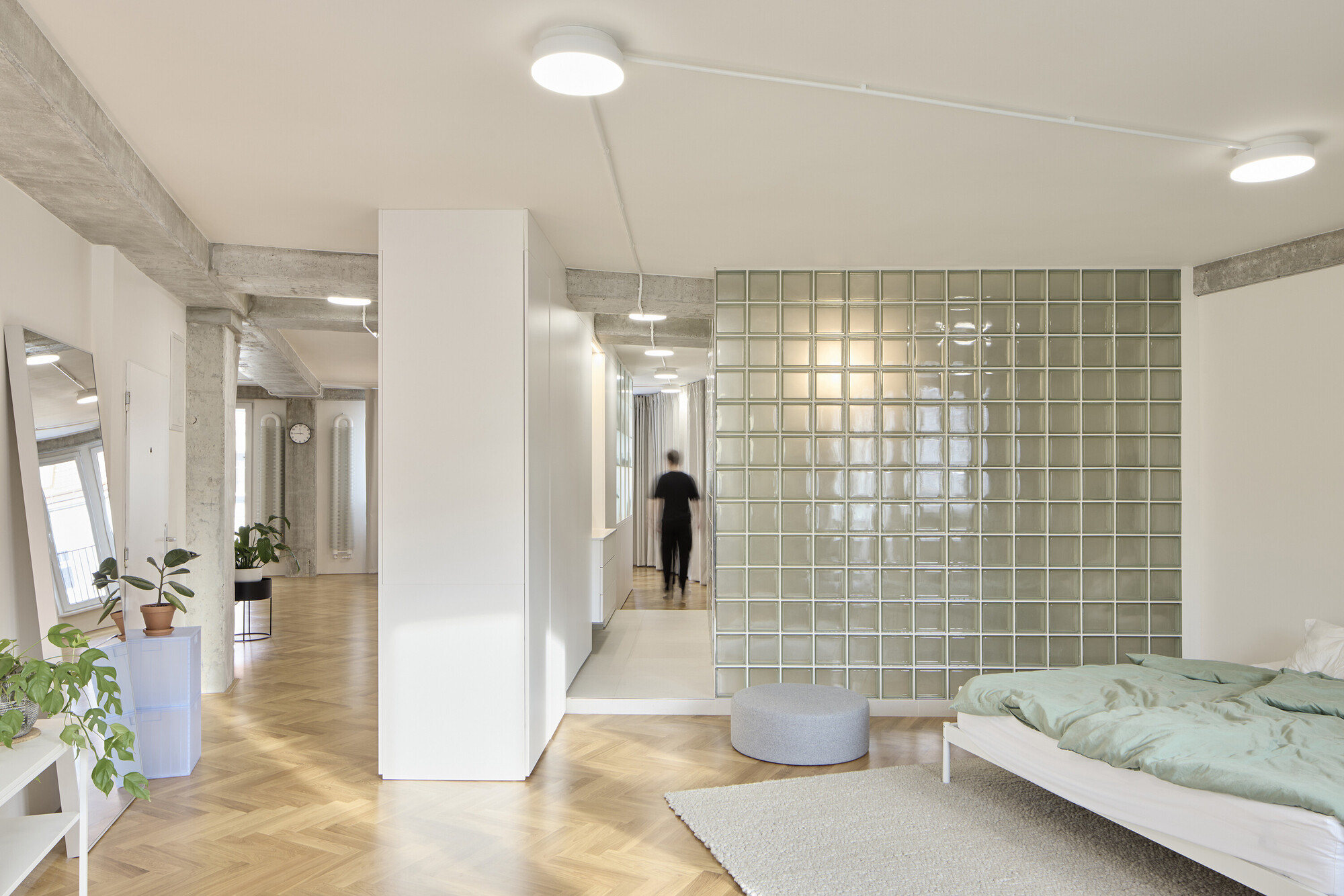 Bedroom with translucent glass block wall and a figure walking down the corridor beyond