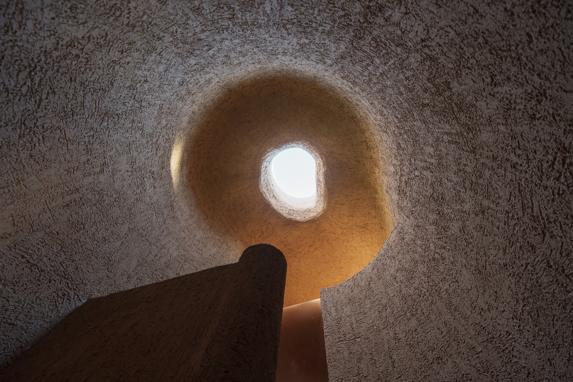 Upward view through a circular skylight opening in a textured earthen dome with a single pendant light