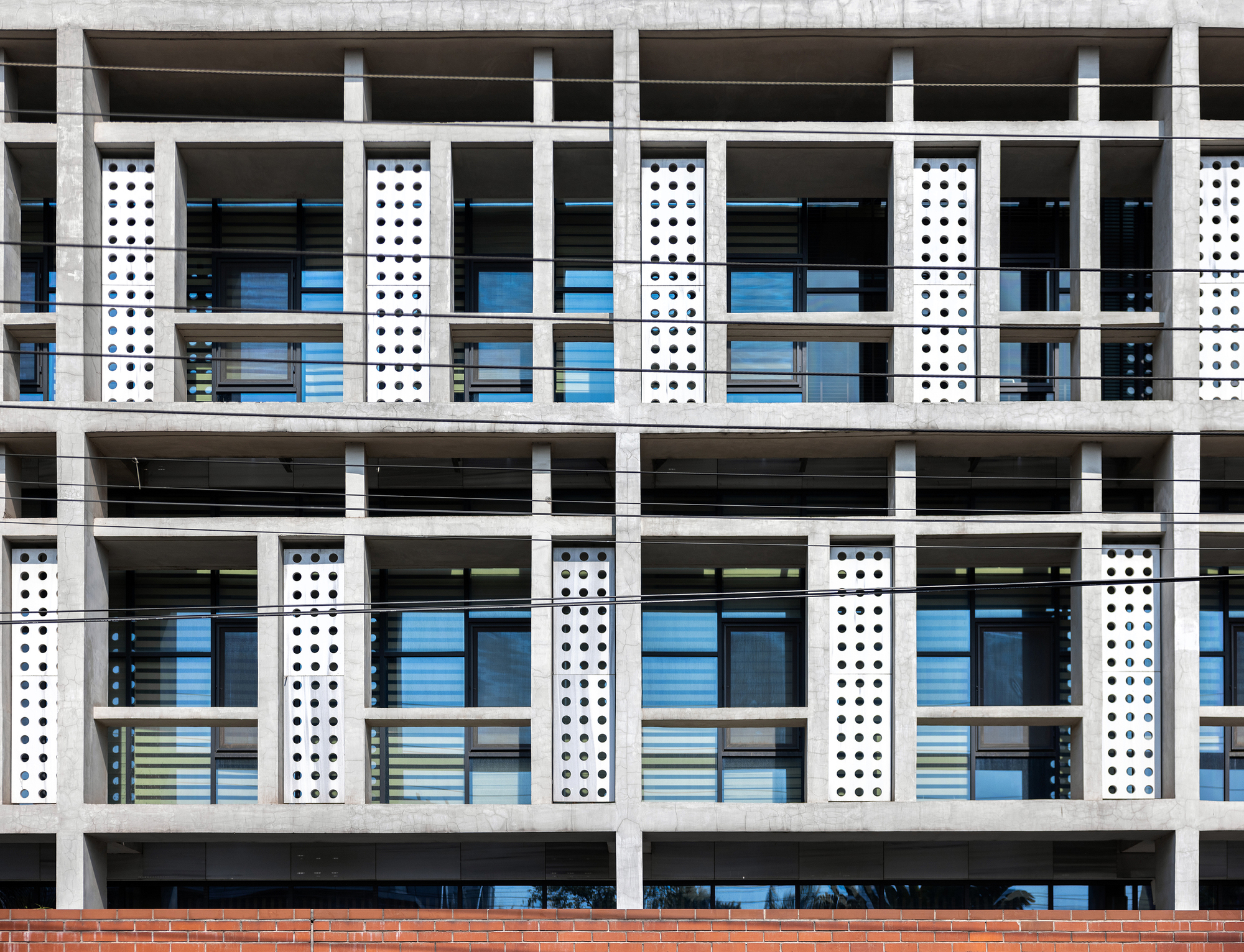 Close-up of the white concrete frame facade showing perforated vertical panels and horizontal floor slabs