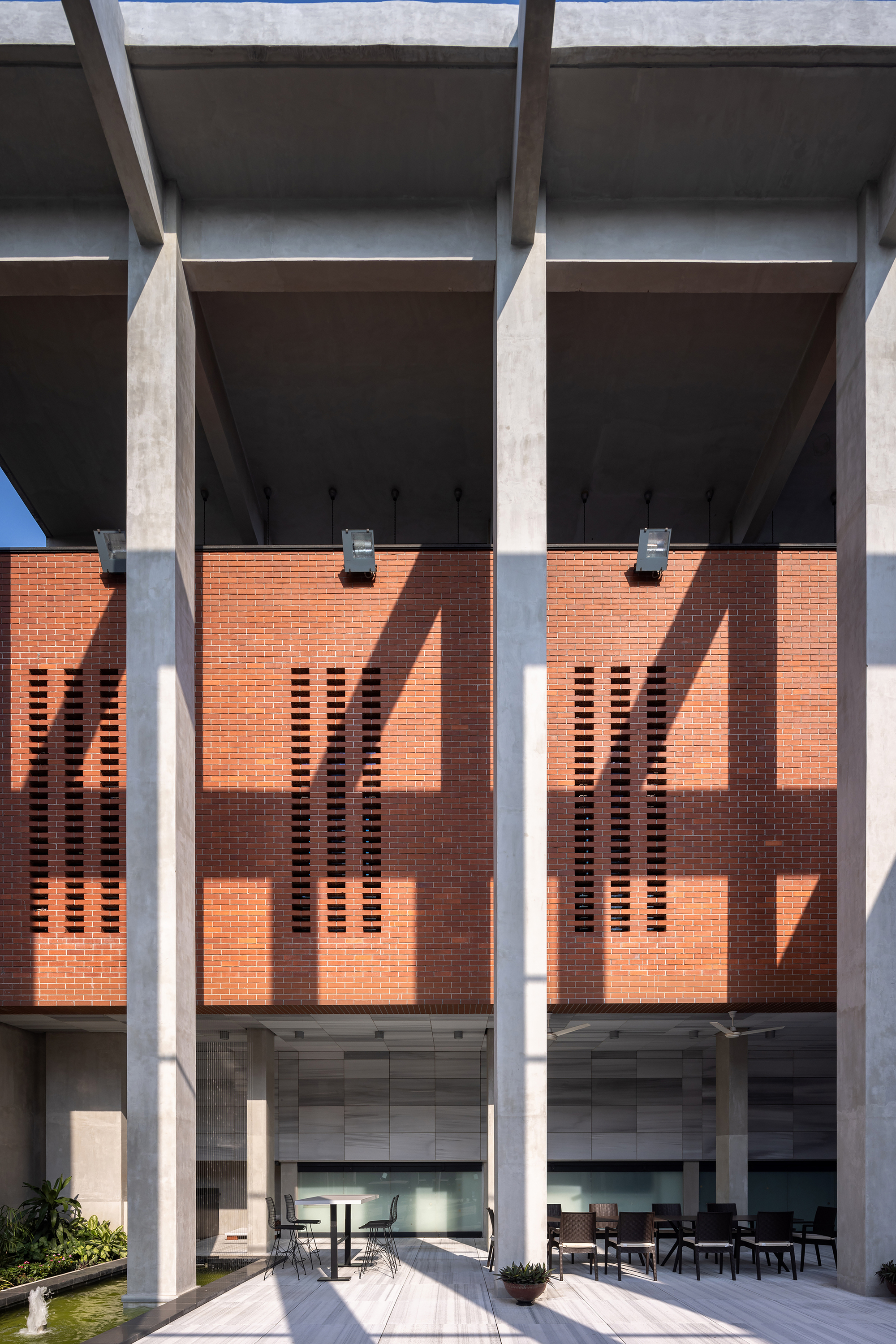 Perforated brick screen wall behind concrete columns casting sharp shadows in bright sunlight