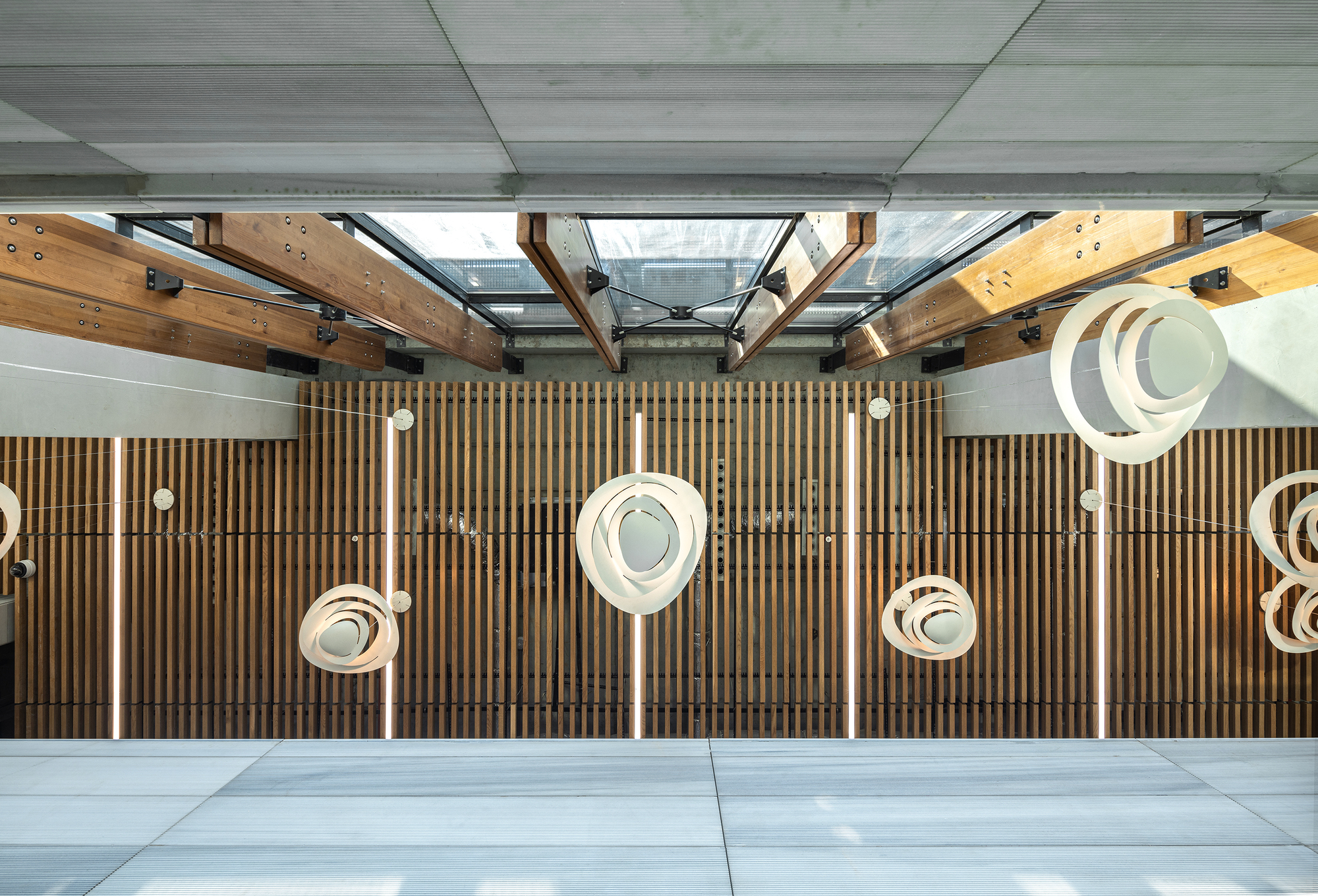Top-down view of a timber-slatted wall with suspended circular pendant lights and exposed steel roof trusses