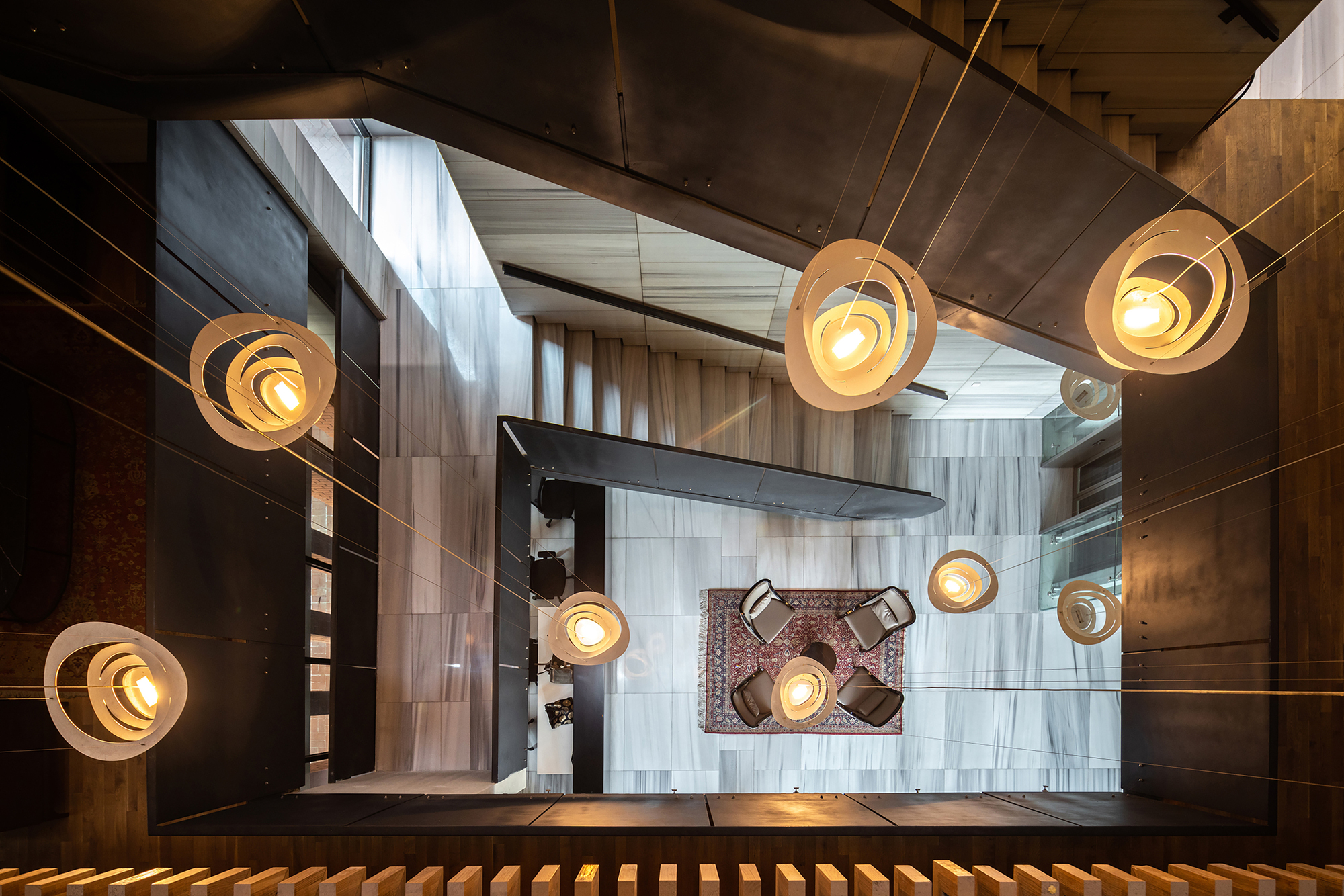 Looking down the stairwell with tiered pendant lights illuminating mixed material walls and tiled floors