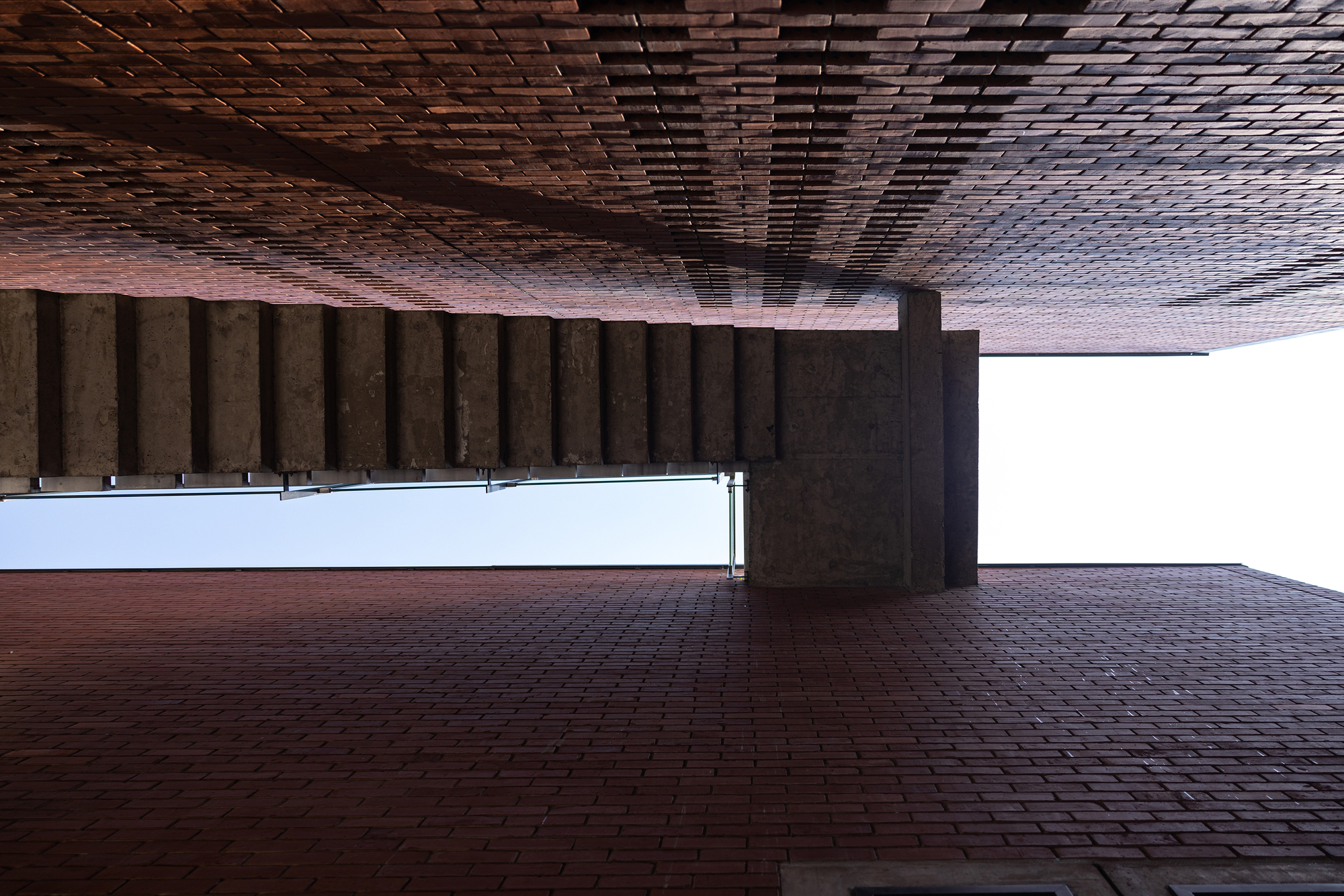 Covered brick courtyard with patterned timber ceiling and concrete columns framing the open plaza