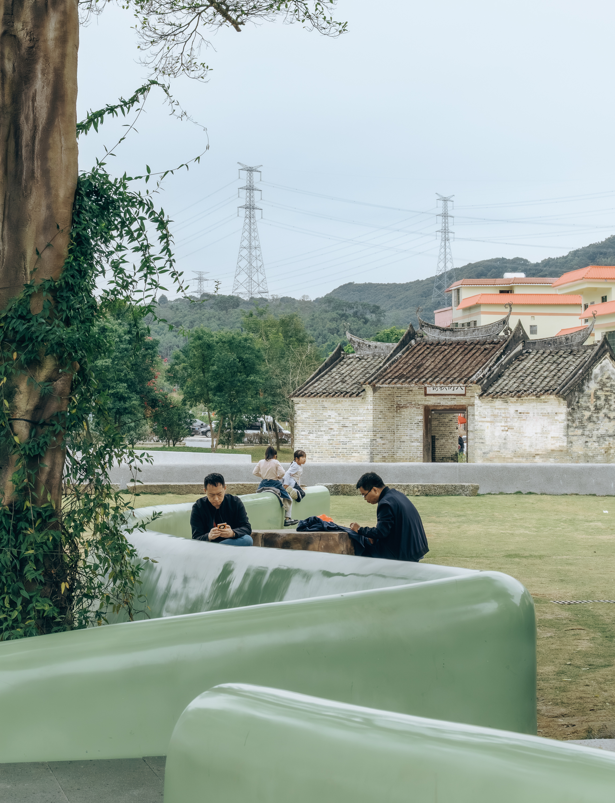 Curved pale green seating elements with visitors amid trees and a historic stone building beyond