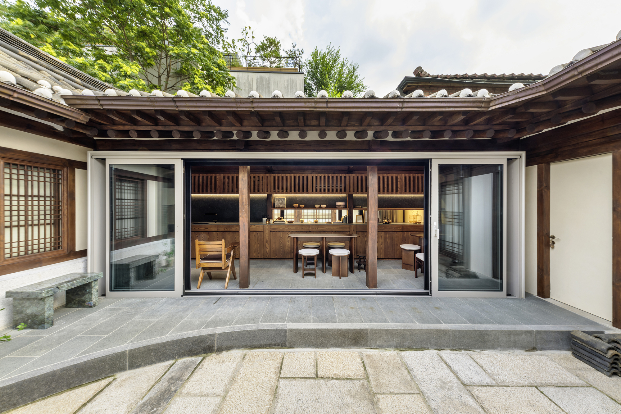 Courtyard view through open sliding glass doors into a timber kitchen with exposed rafter ceiling
