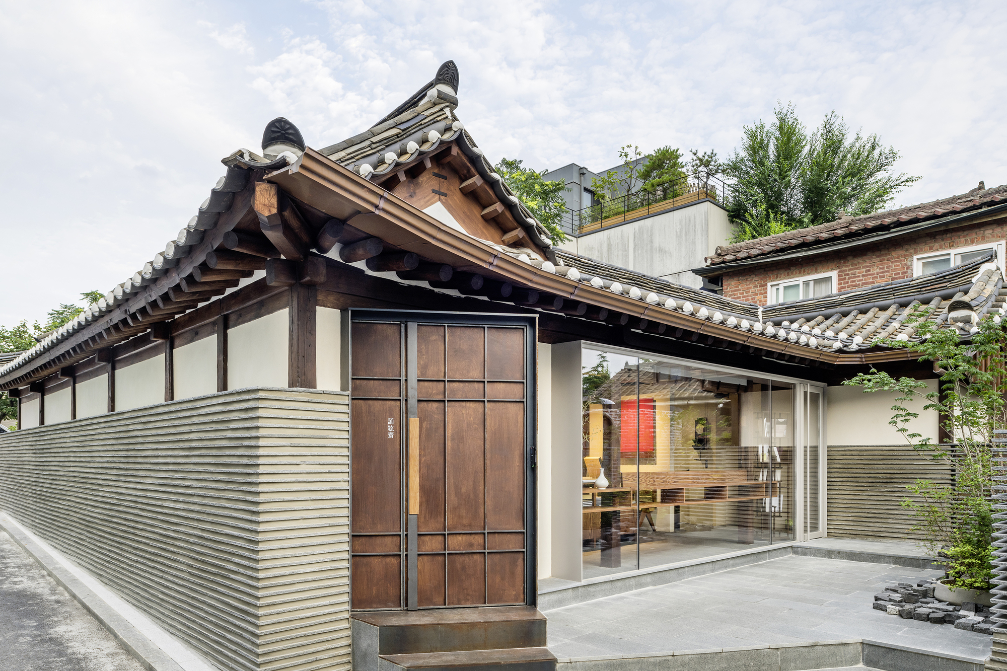 Exterior view of the renovated hanok with traditional tiled roof and ribbed metal facade under cloudy skies