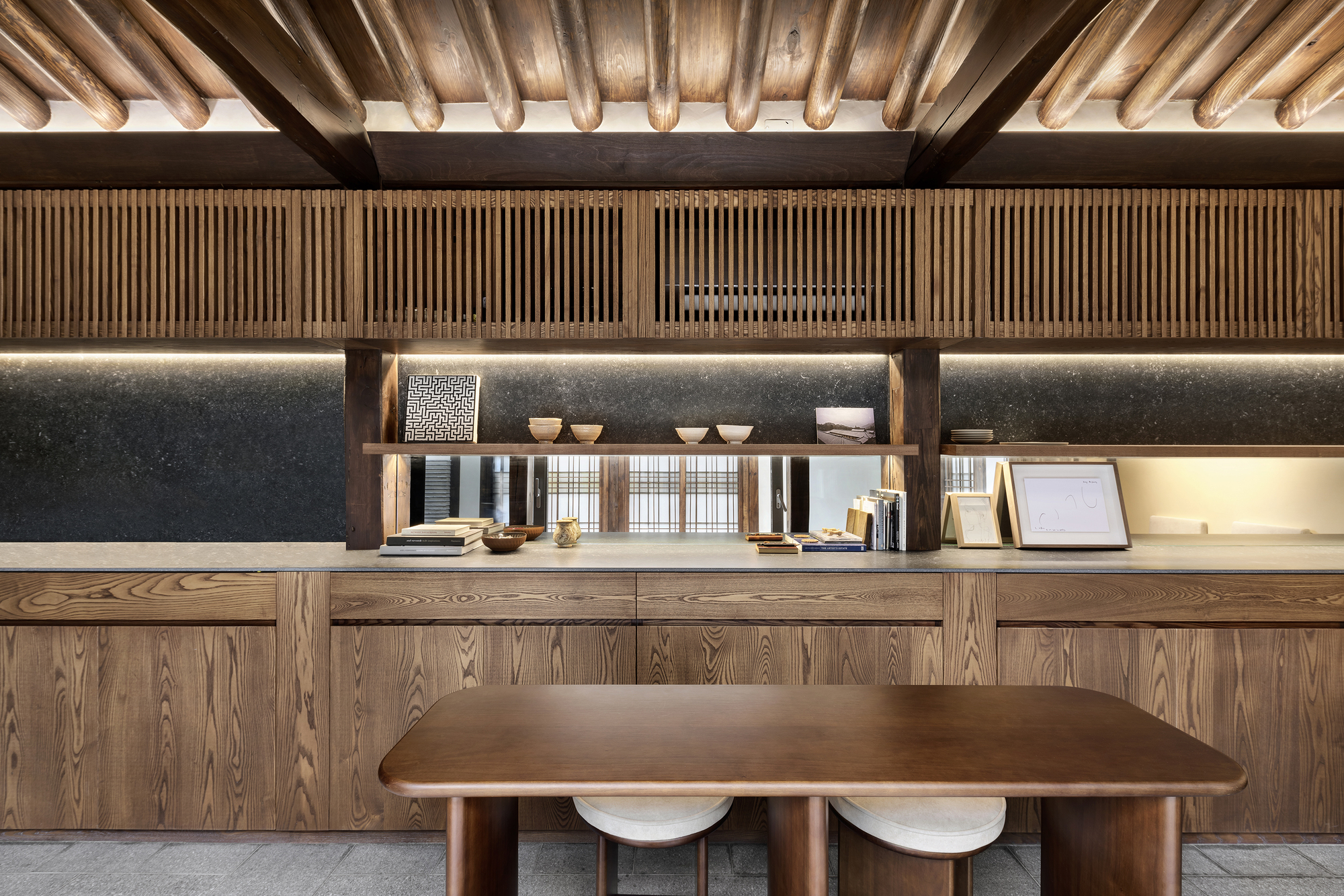 Kitchen workspace with timber counter, vertical slatted wall panels and exposed ceiling beams with indirect lighting