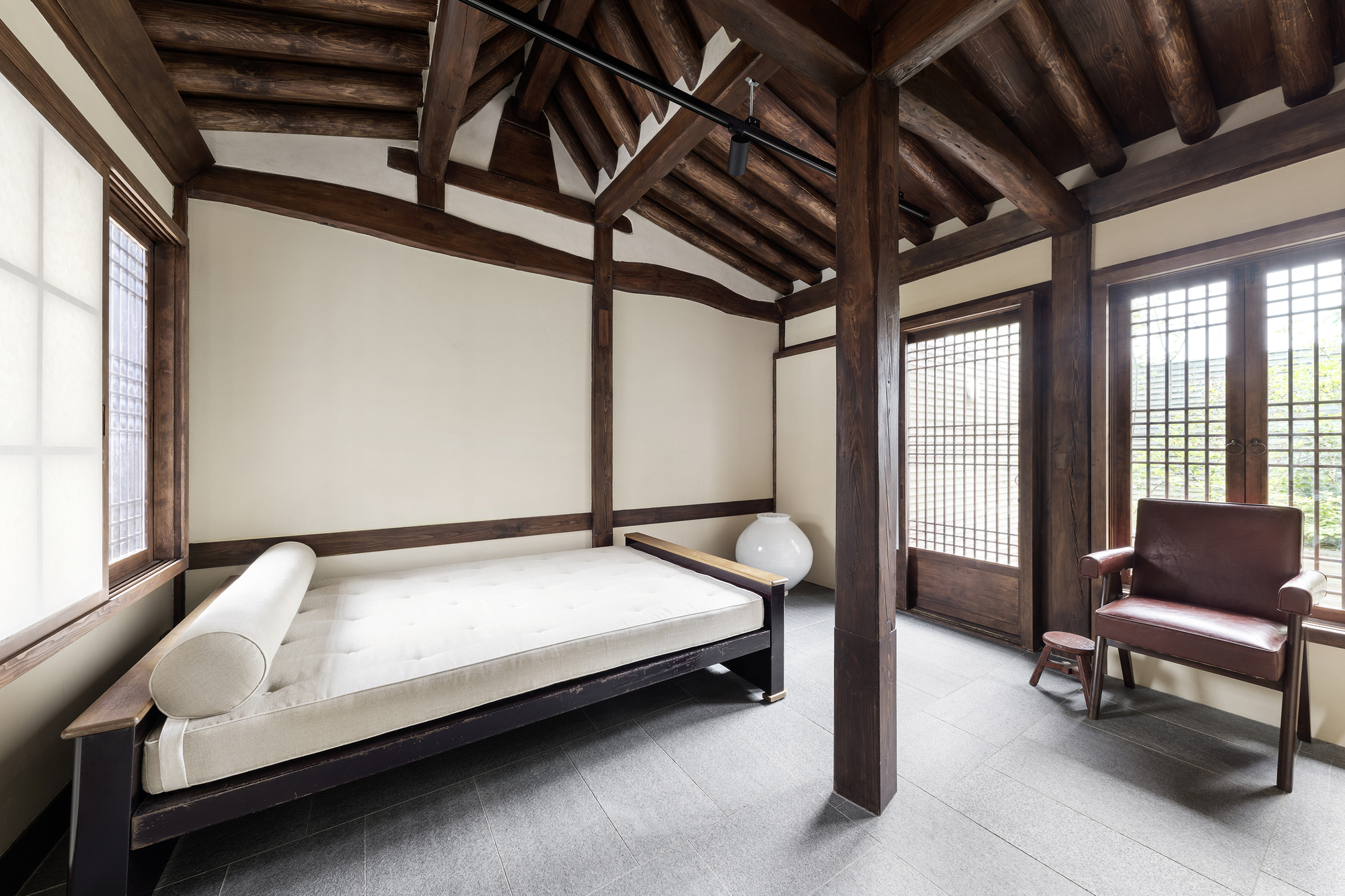 Bedroom with exposed timber post-and-beam structure, gridded sliding doors and white daybed beneath vaulted ceiling