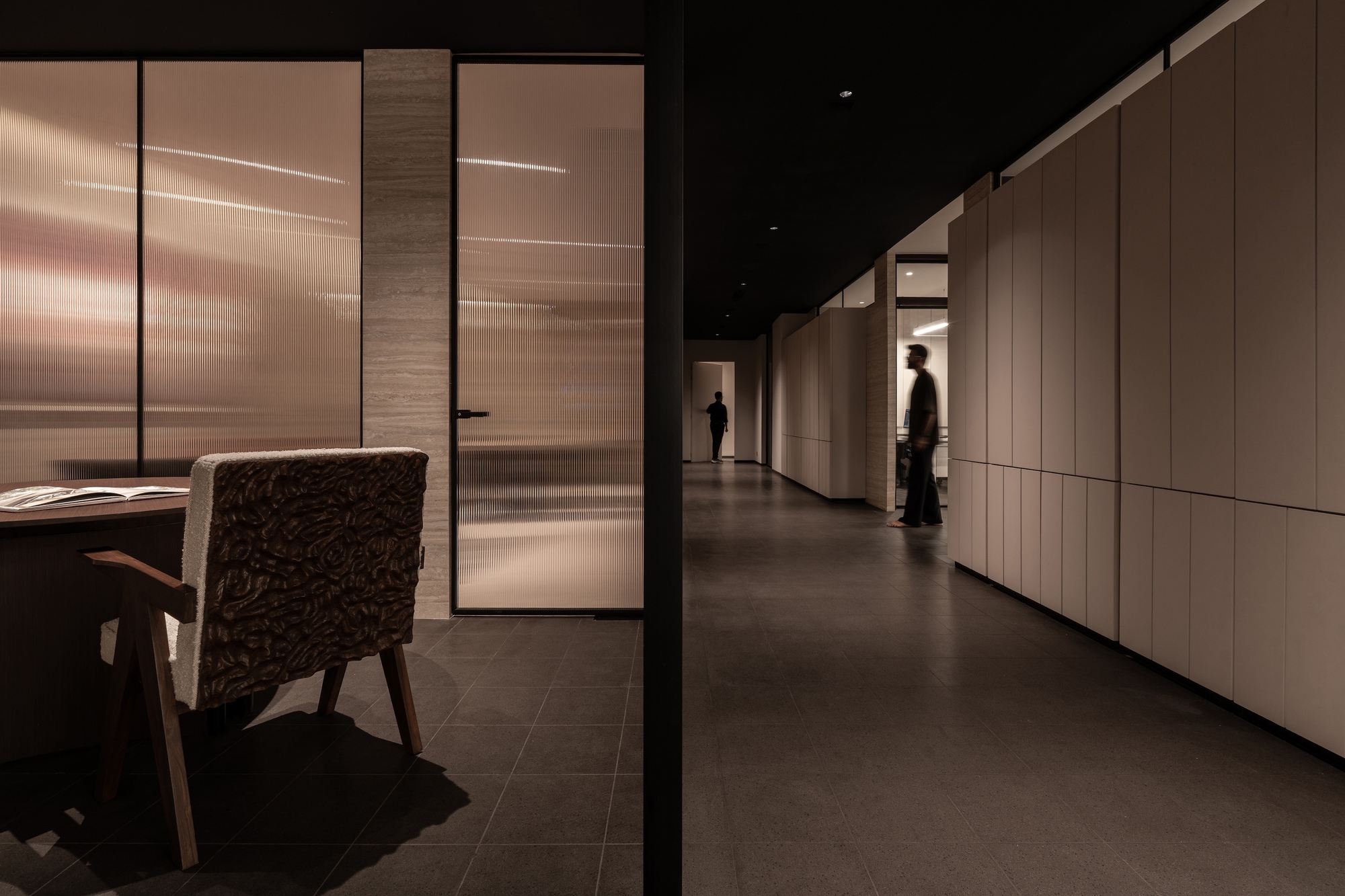 Long corridor with translucent glass partitions and light wood paneling under dramatic artificial lighting