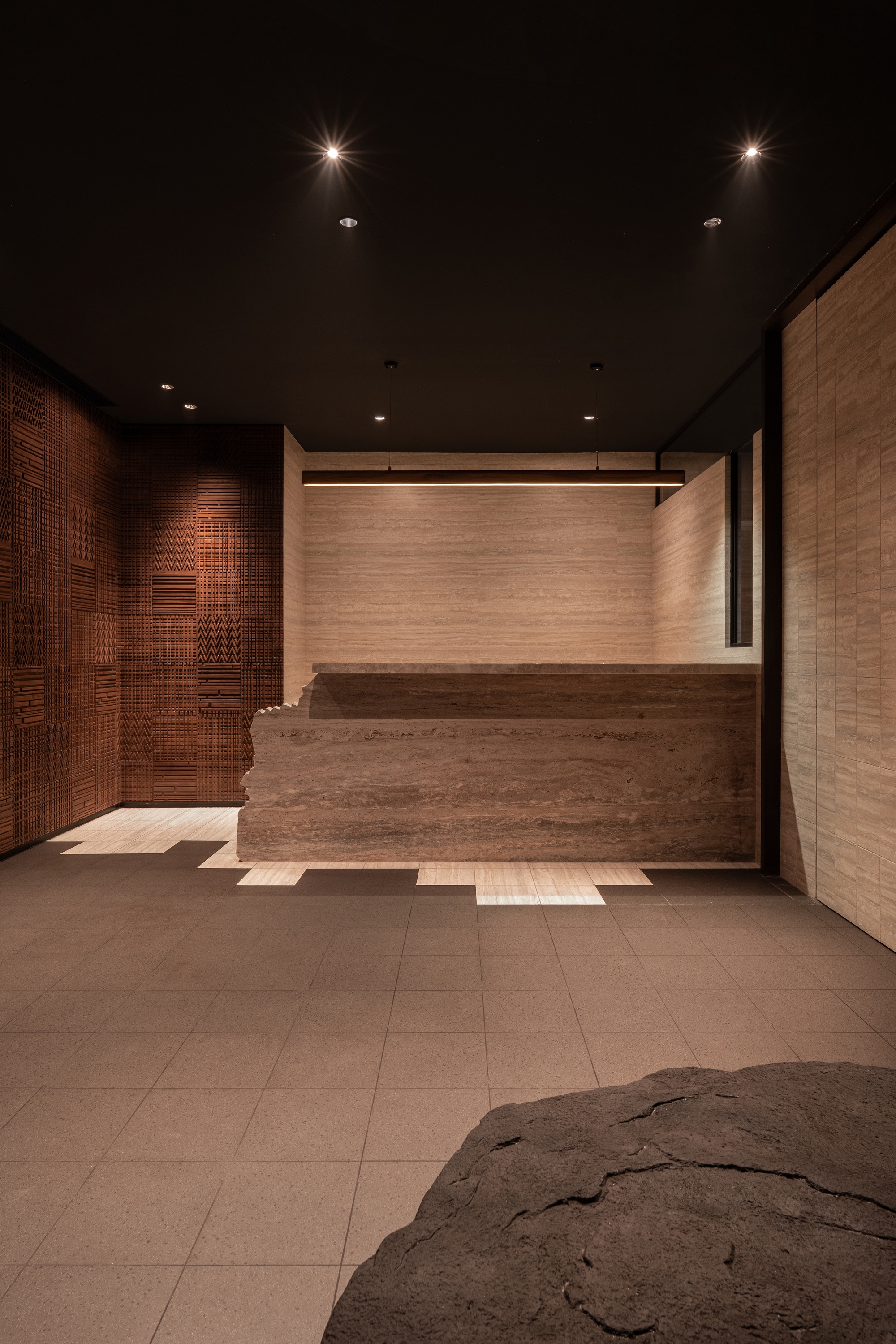 Reception desk in travertine stone with textured copper wall panels and recessed ceiling lighting