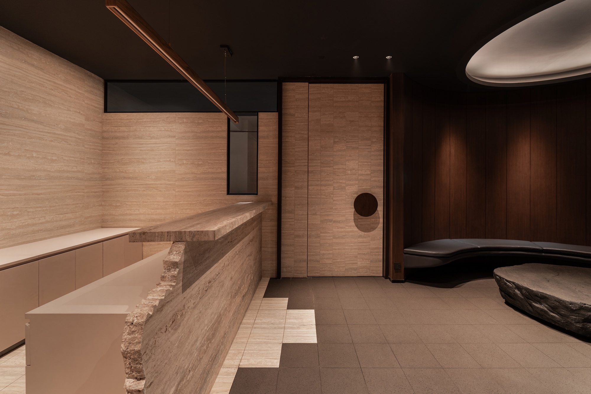 Layered travertine reception desk with rough-hewn edges beneath horizontal timber wall panels and dark ceiling