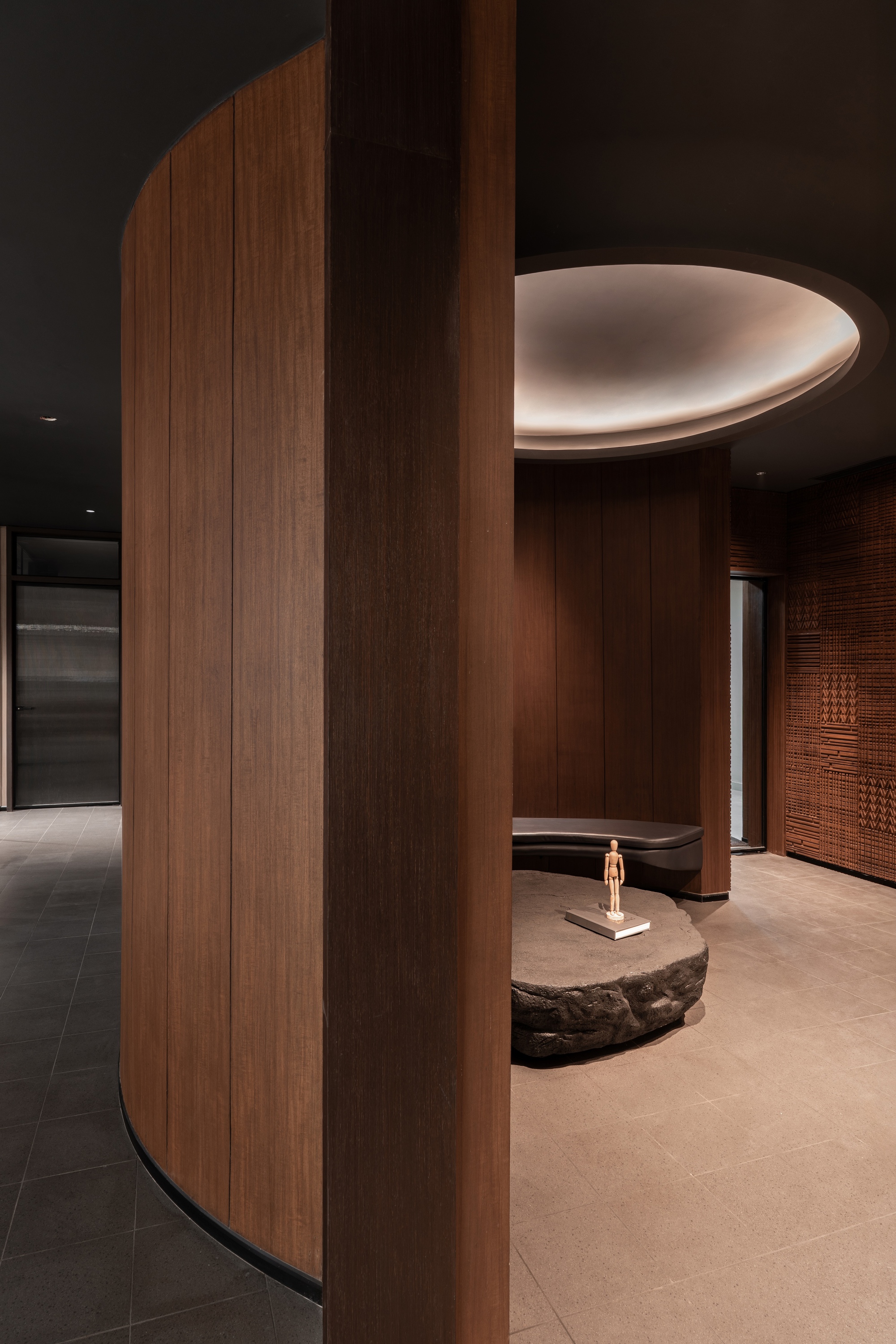 Curved wood-clad column beside a circular recessed ceiling light above a lobby seating area