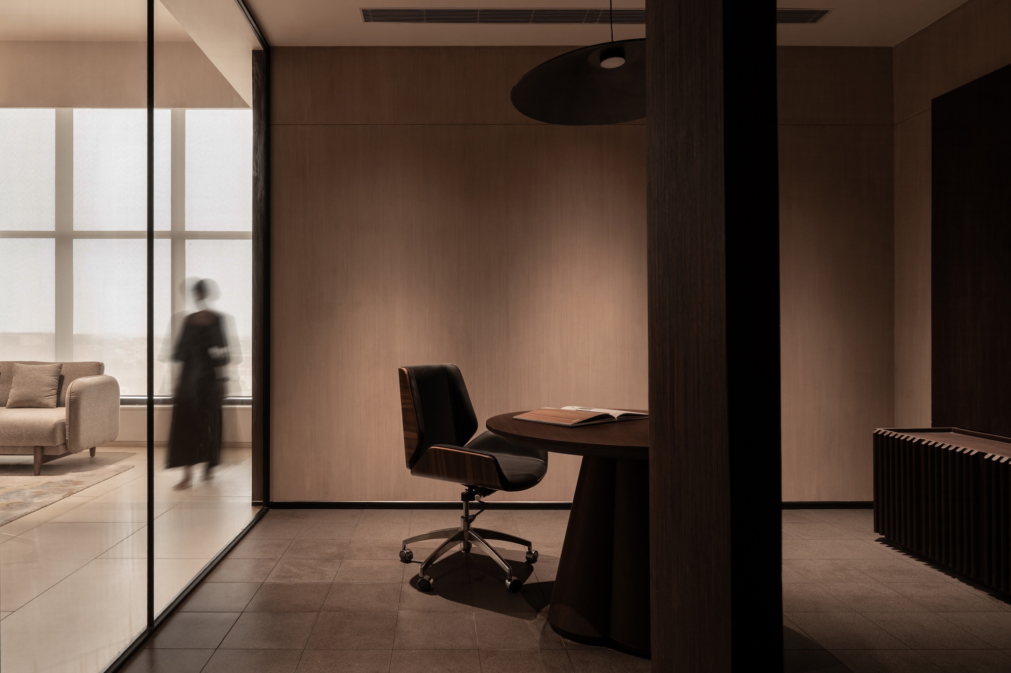 Private office alcove with circular desk and framed glass partition as a figure passes by
