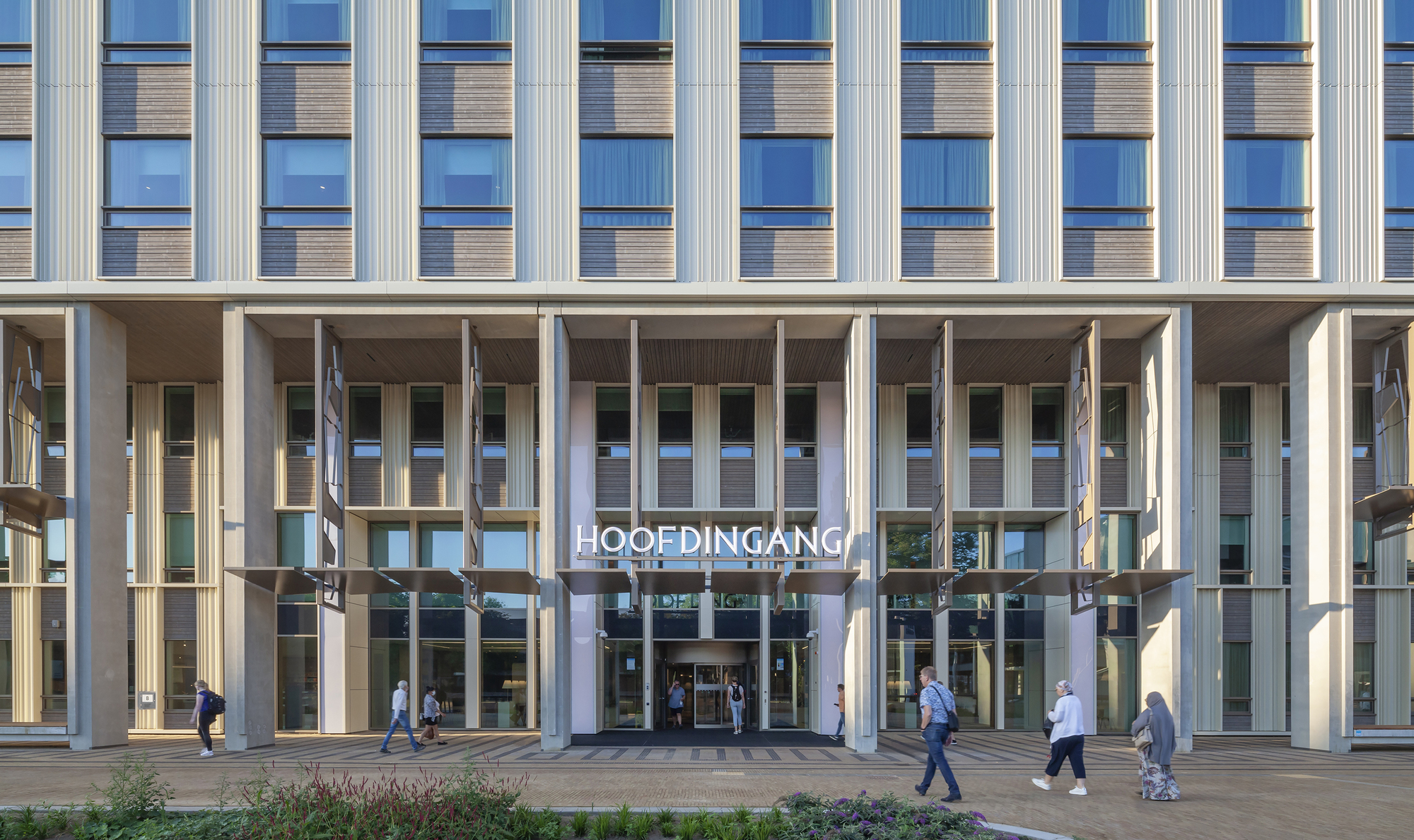 Ground-level entrance colonnade with vertical fins above and pedestrians crossing the plaza