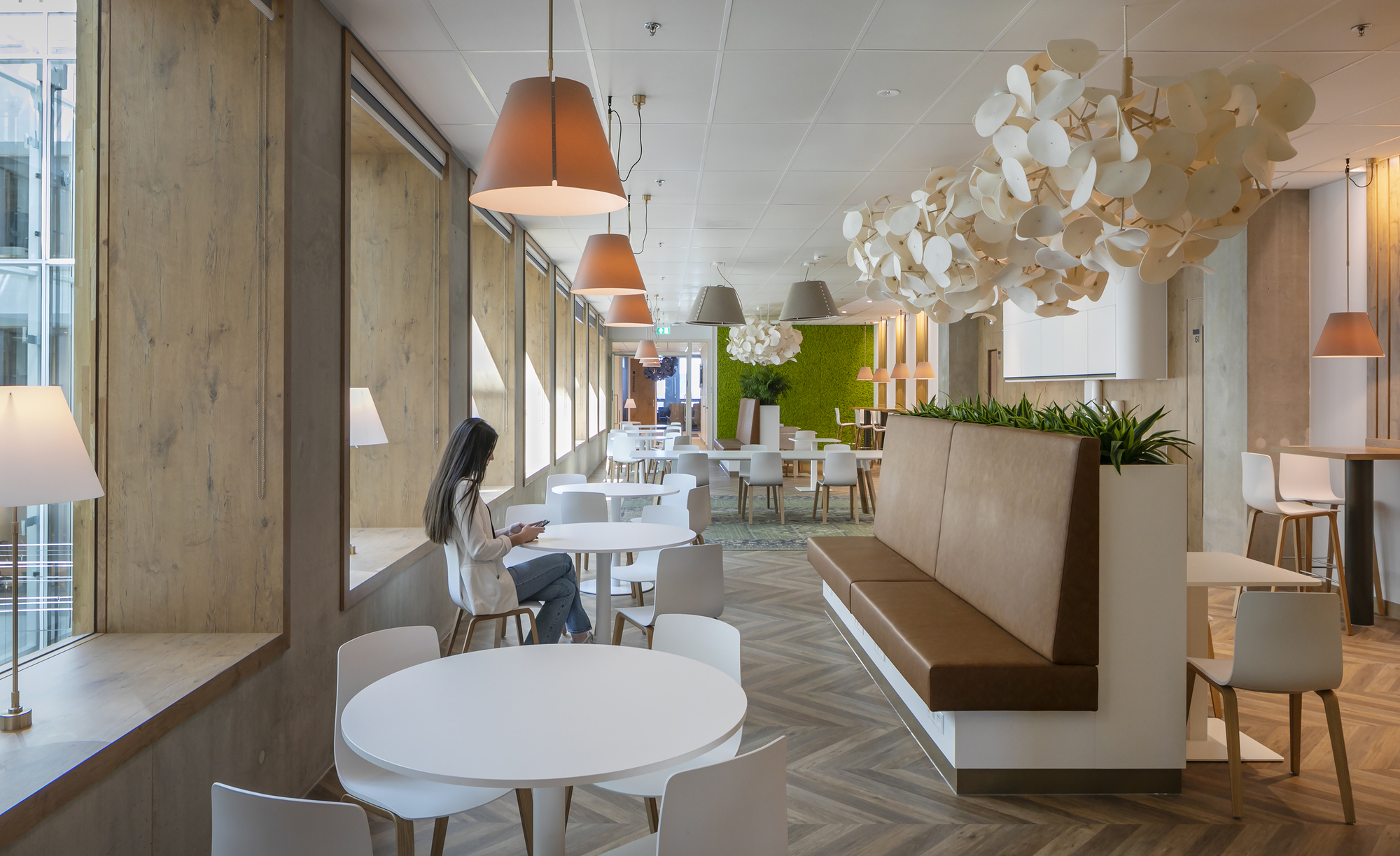 Dining area with round white tables, timber-paneled walls and pendant lighting beside glazed curtain wall