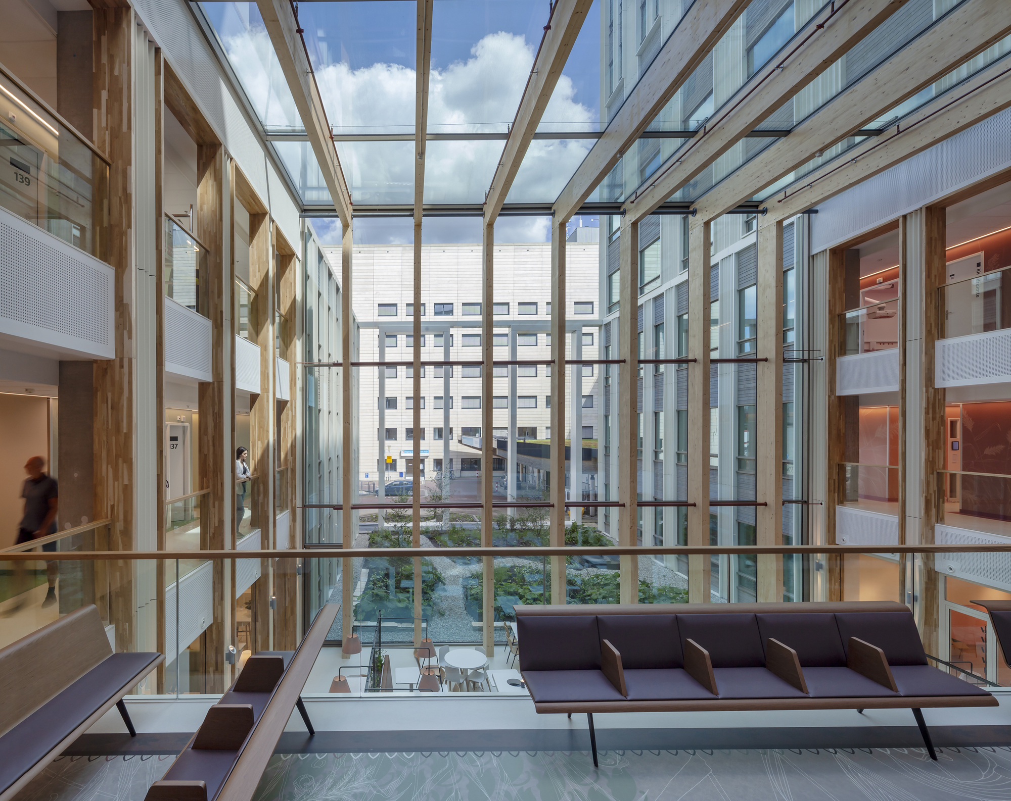 Lounge seating with dark upholstery facing floor-to-ceiling glazing overlooking a landscaped courtyard between buildings