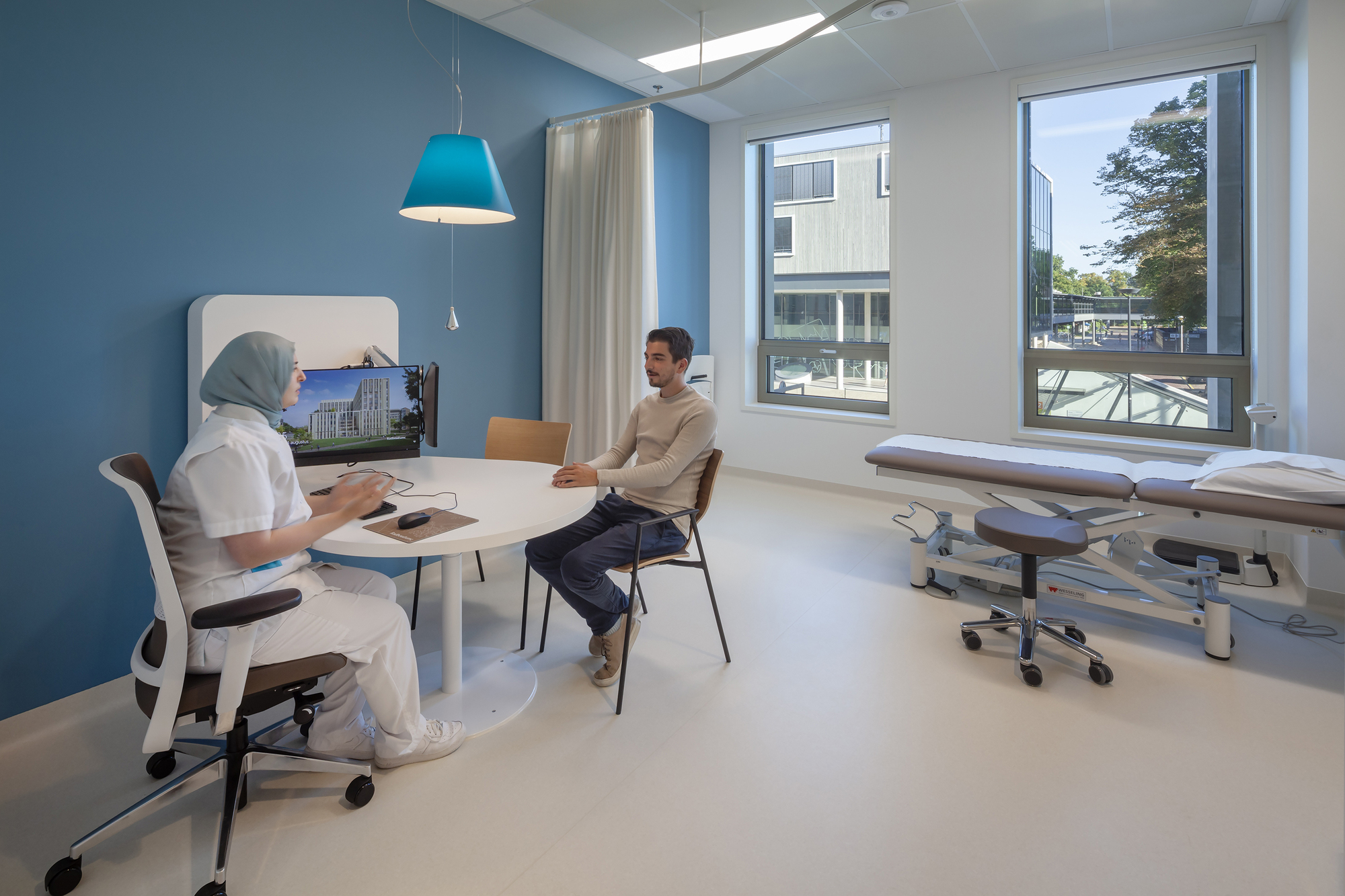 Consultation room with pale blue walls and tall windows overlooking trees outside