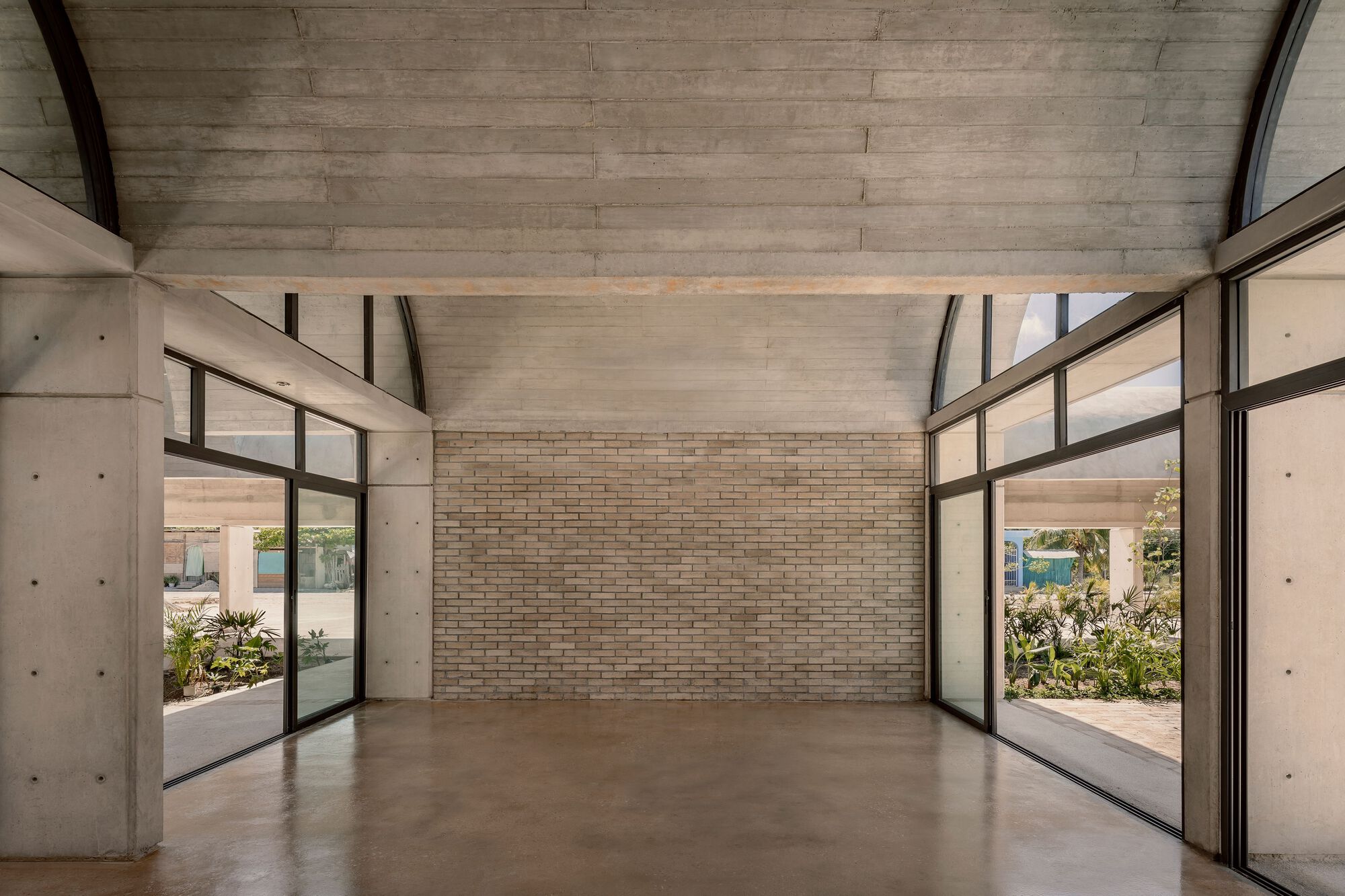 Interior room with vaulted concrete ceiling, polished concrete floor, and floor-to-ceiling glazed doors on both sides