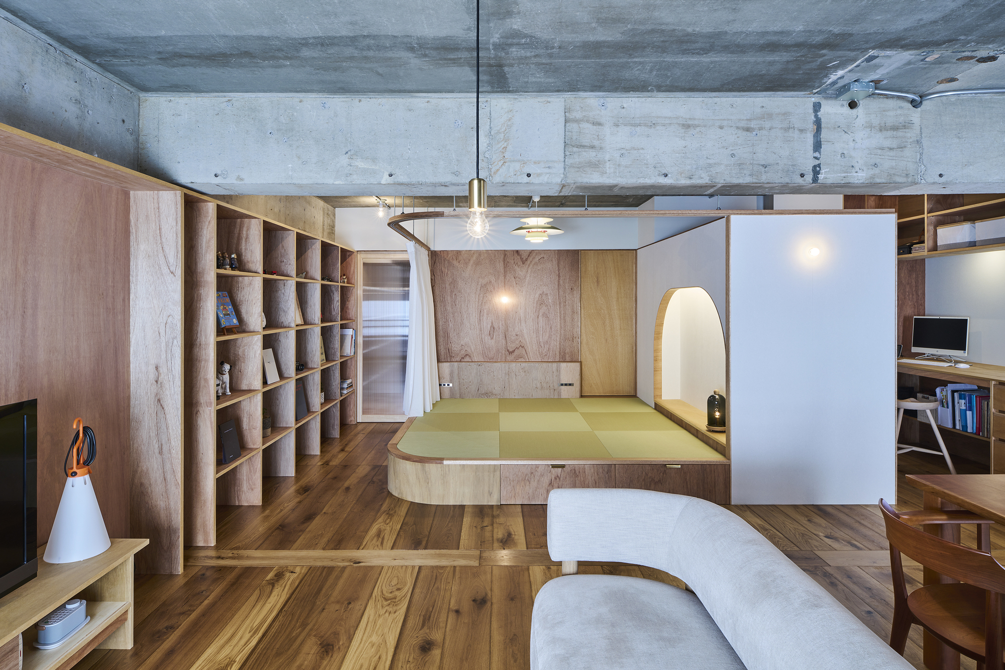 Open-plan interior with raised tatami platform, timber shelving unit, and exposed concrete ceiling