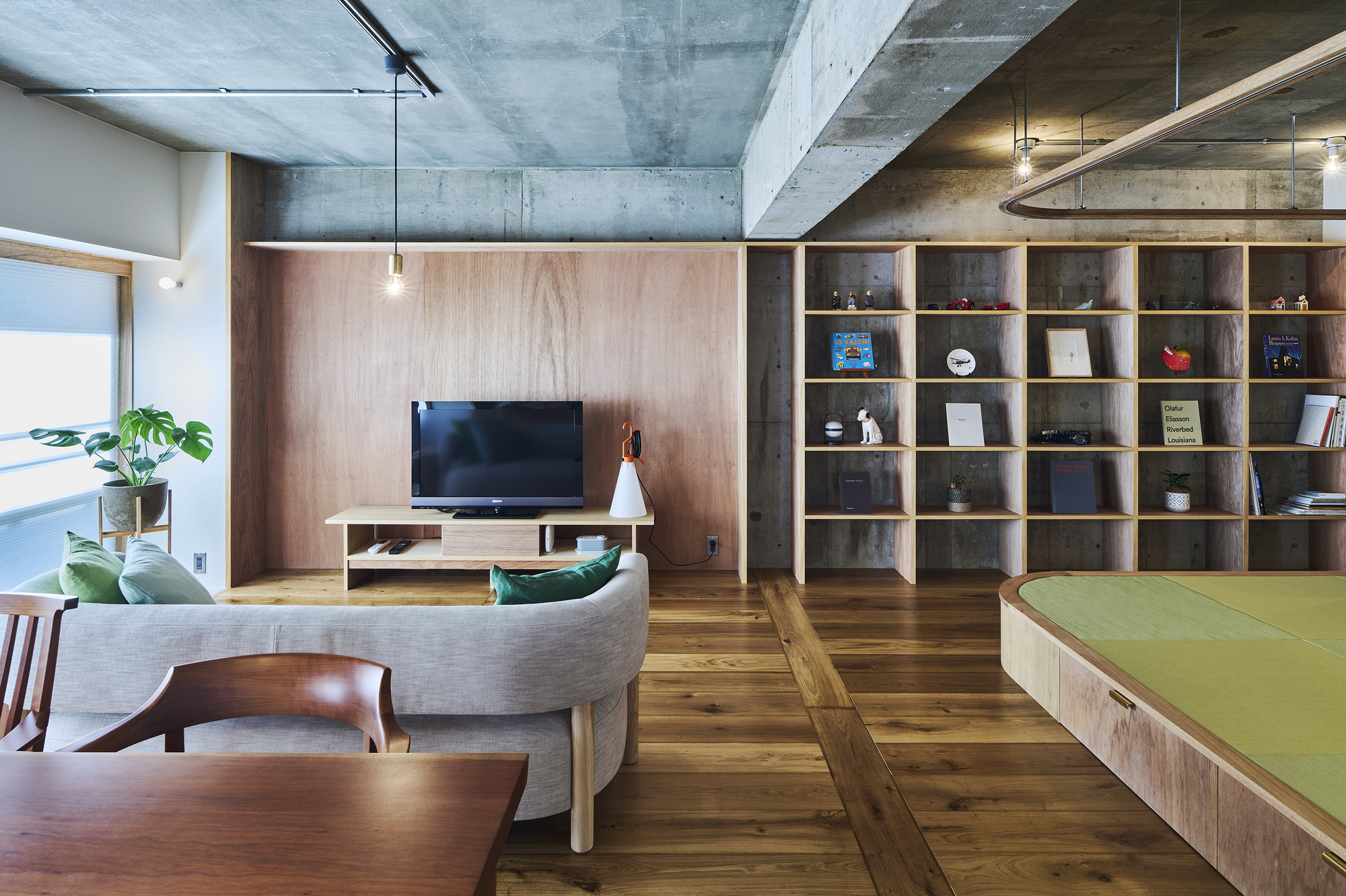 Living area with timber shelving wall, raised tatami platform, and potted plant by the window