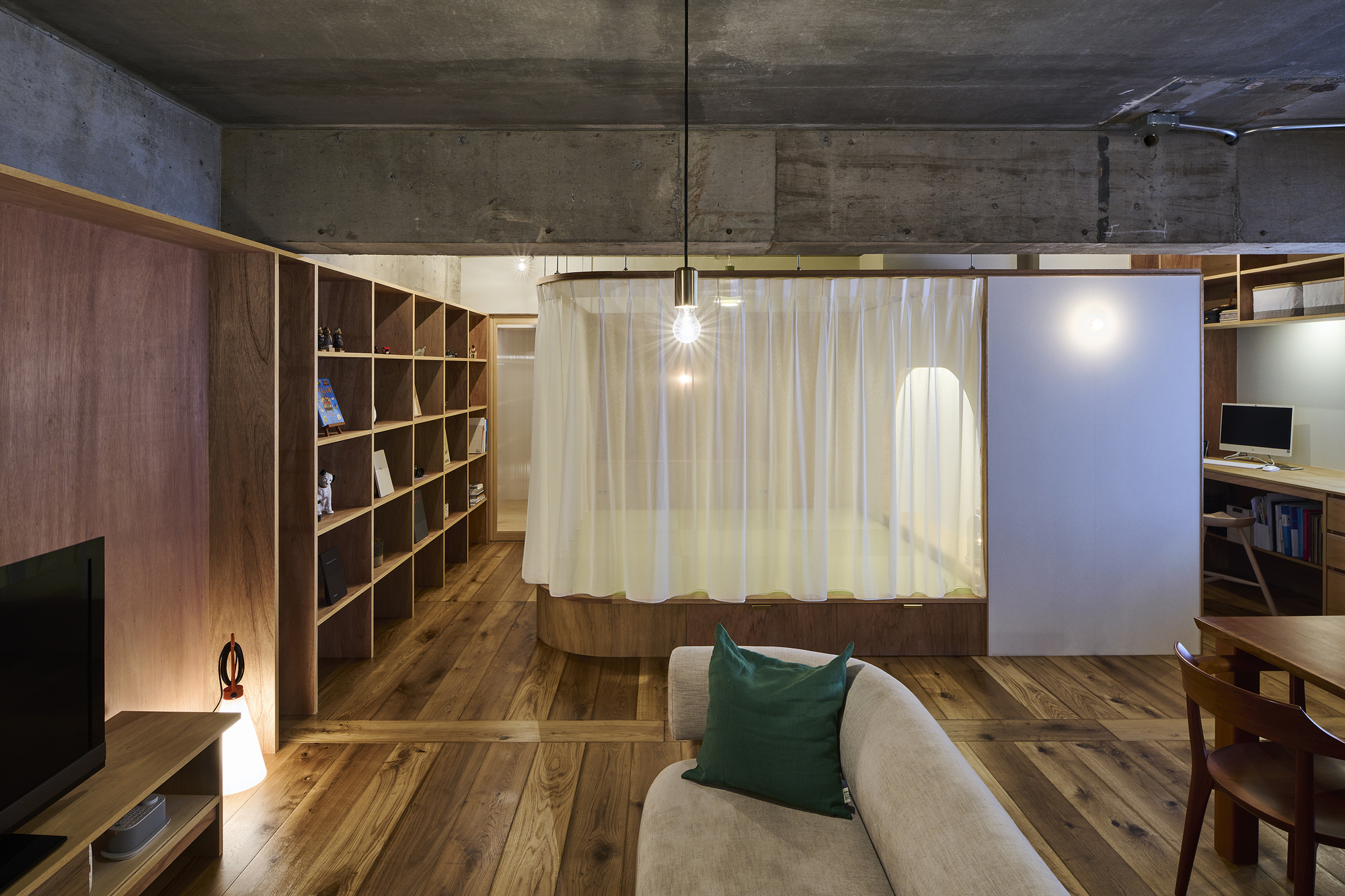 Living space with curved curtain track, timber shelving, and exposed concrete ceiling and beams