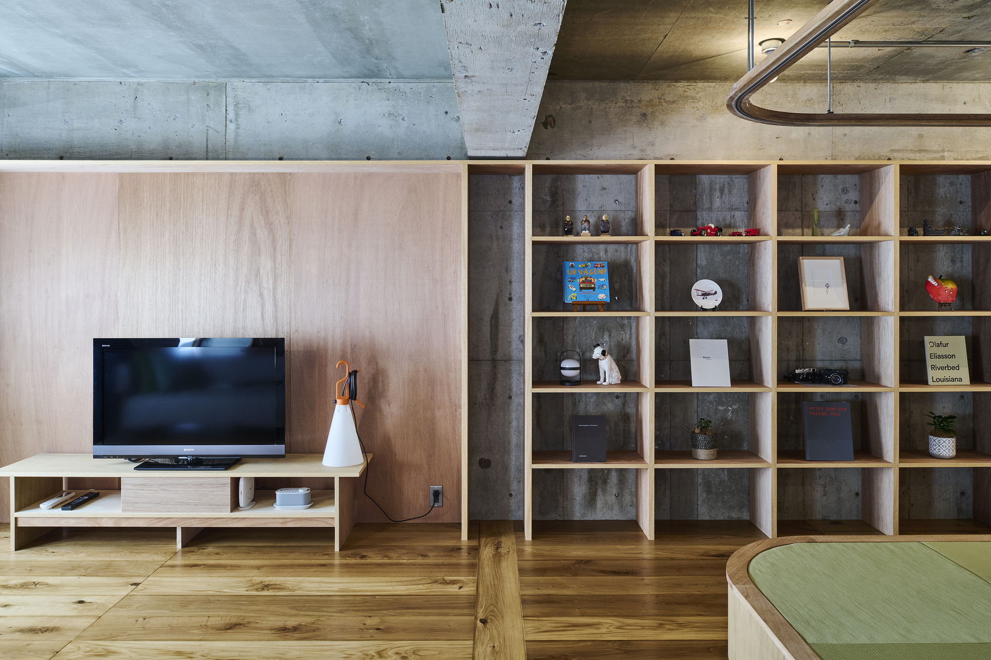 Living area with exposed concrete ceiling, timber shelving grid, and low media console against plywood wall