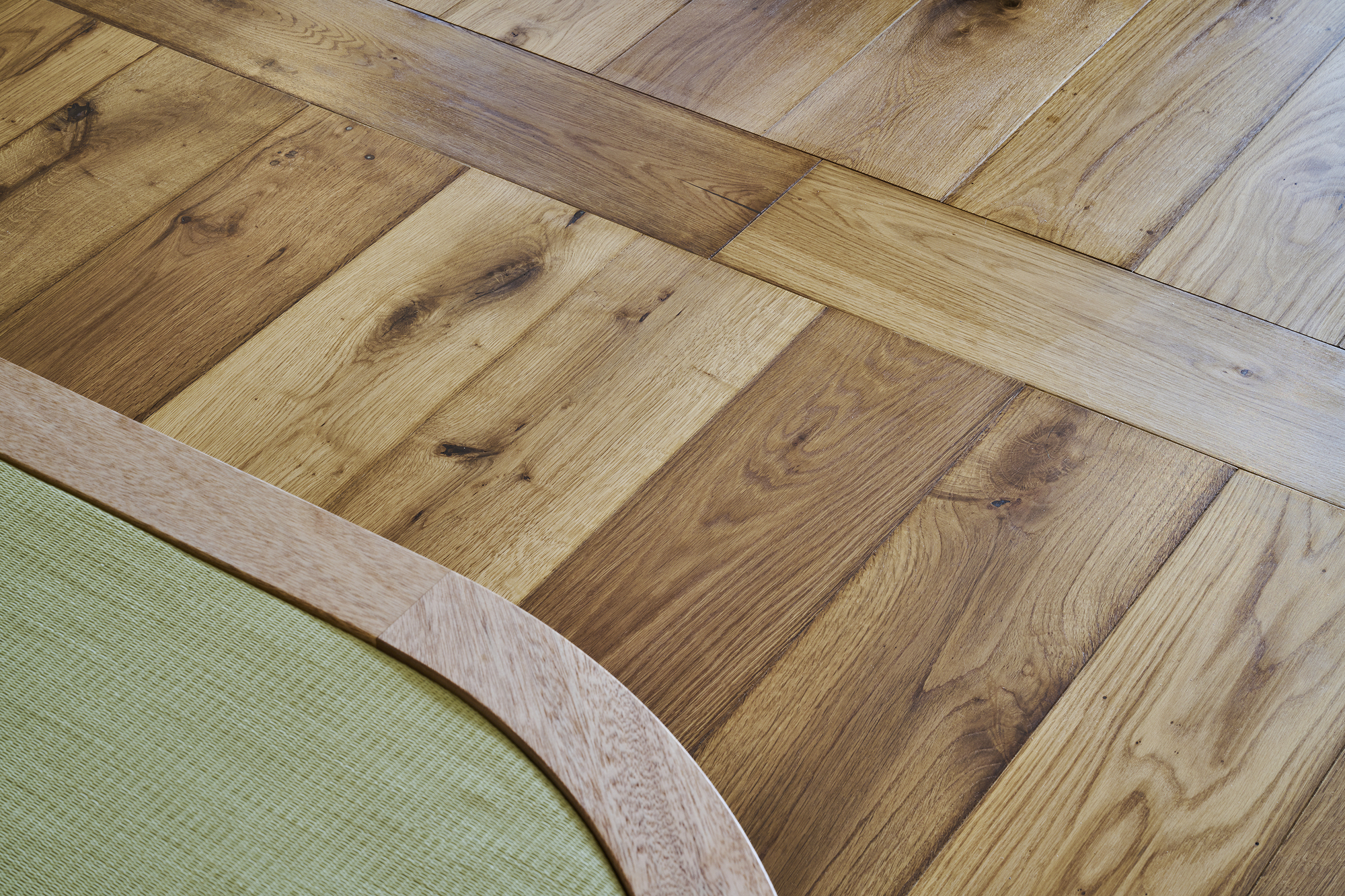 Close-up of reclaimed oak flooring in varied tones meeting the curved edge of a tatami platform