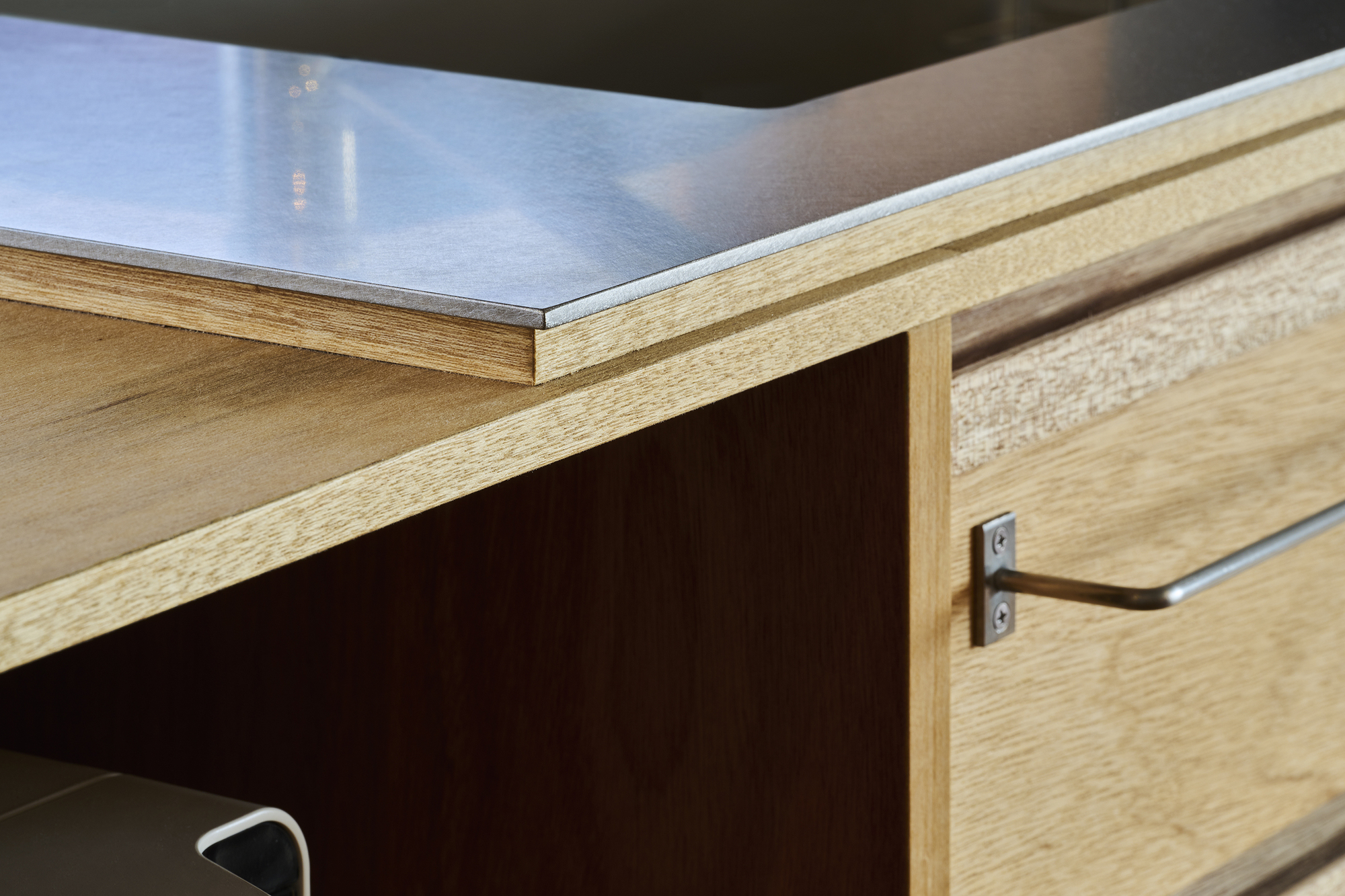 Detail of stainless steel countertop edge meeting an oak drawer front with inset pull hardware