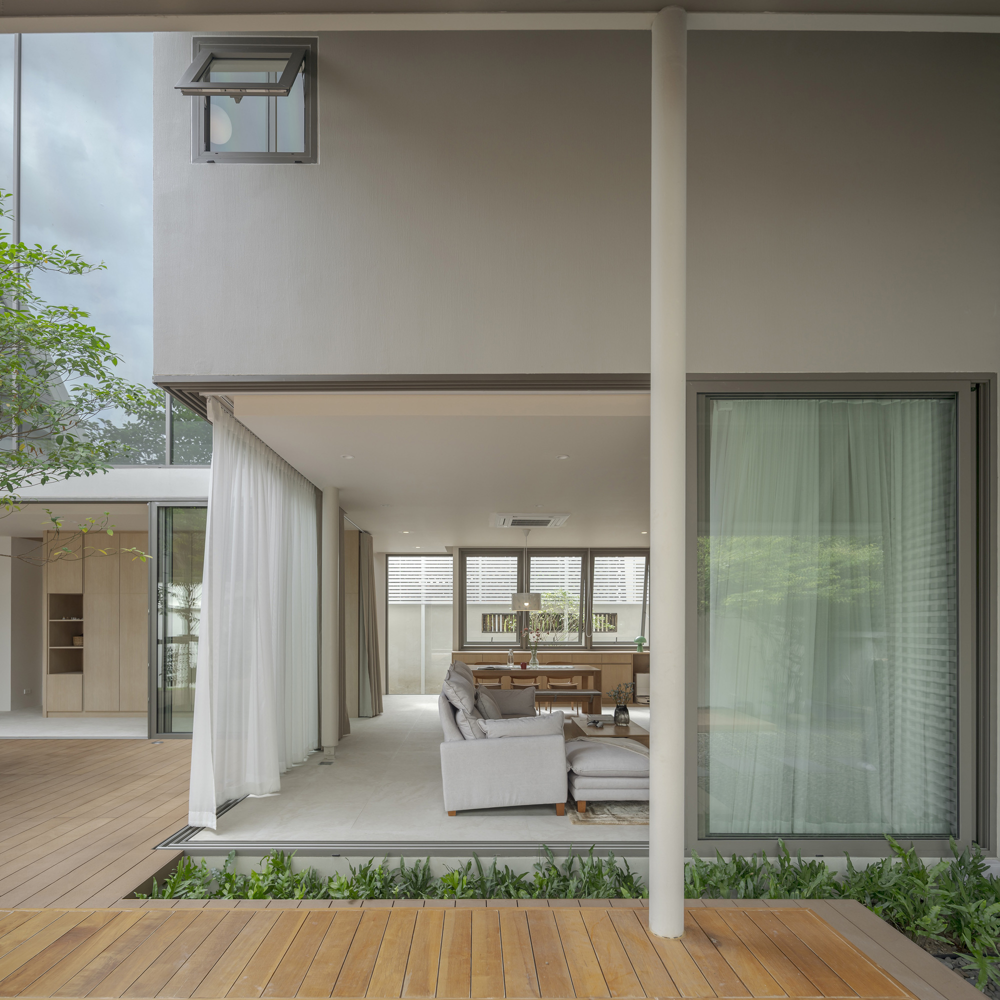 View through courtyard to living and dining space with sheer curtains and planted beds