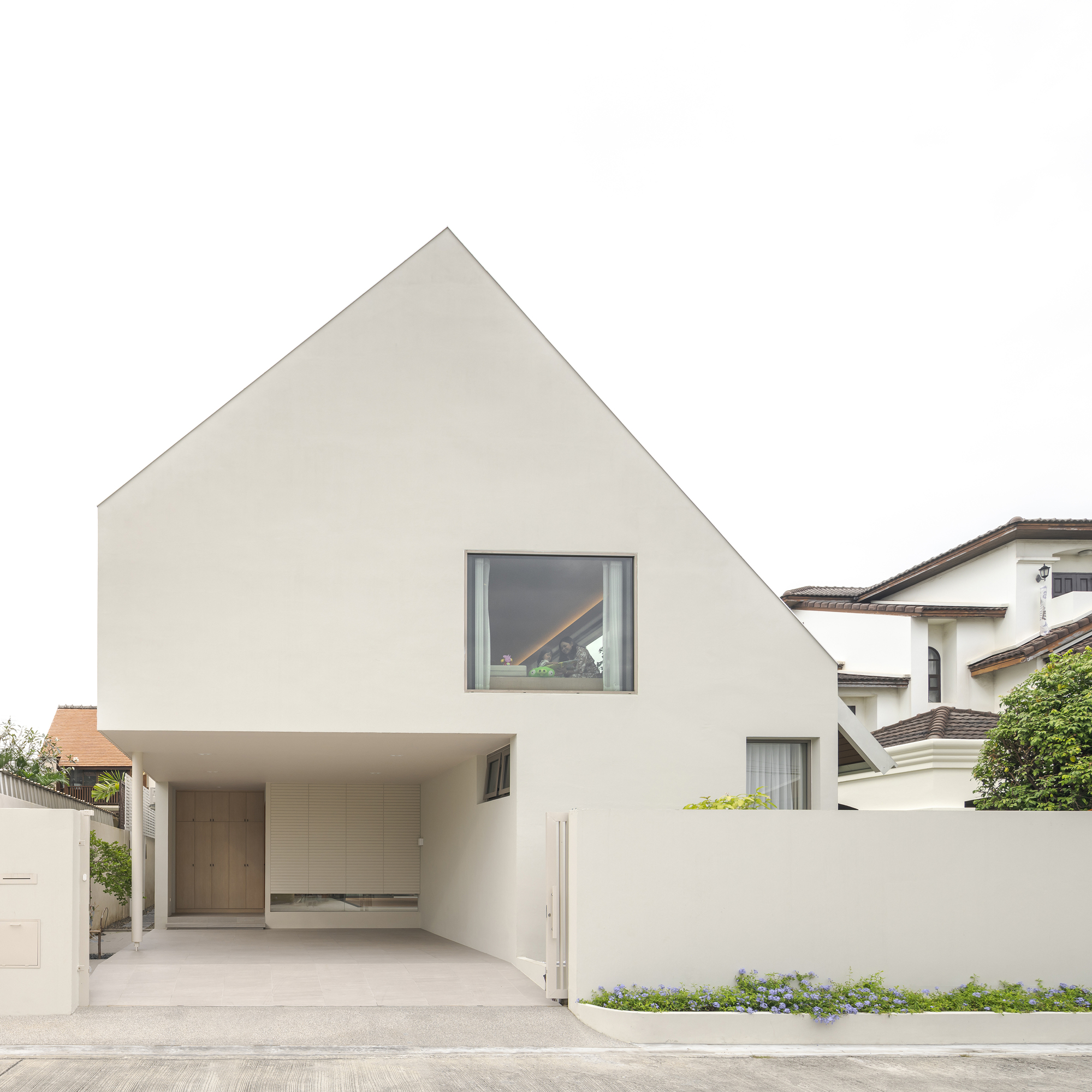 White plastered street facade with gabled profile and covered carport under overcast sky