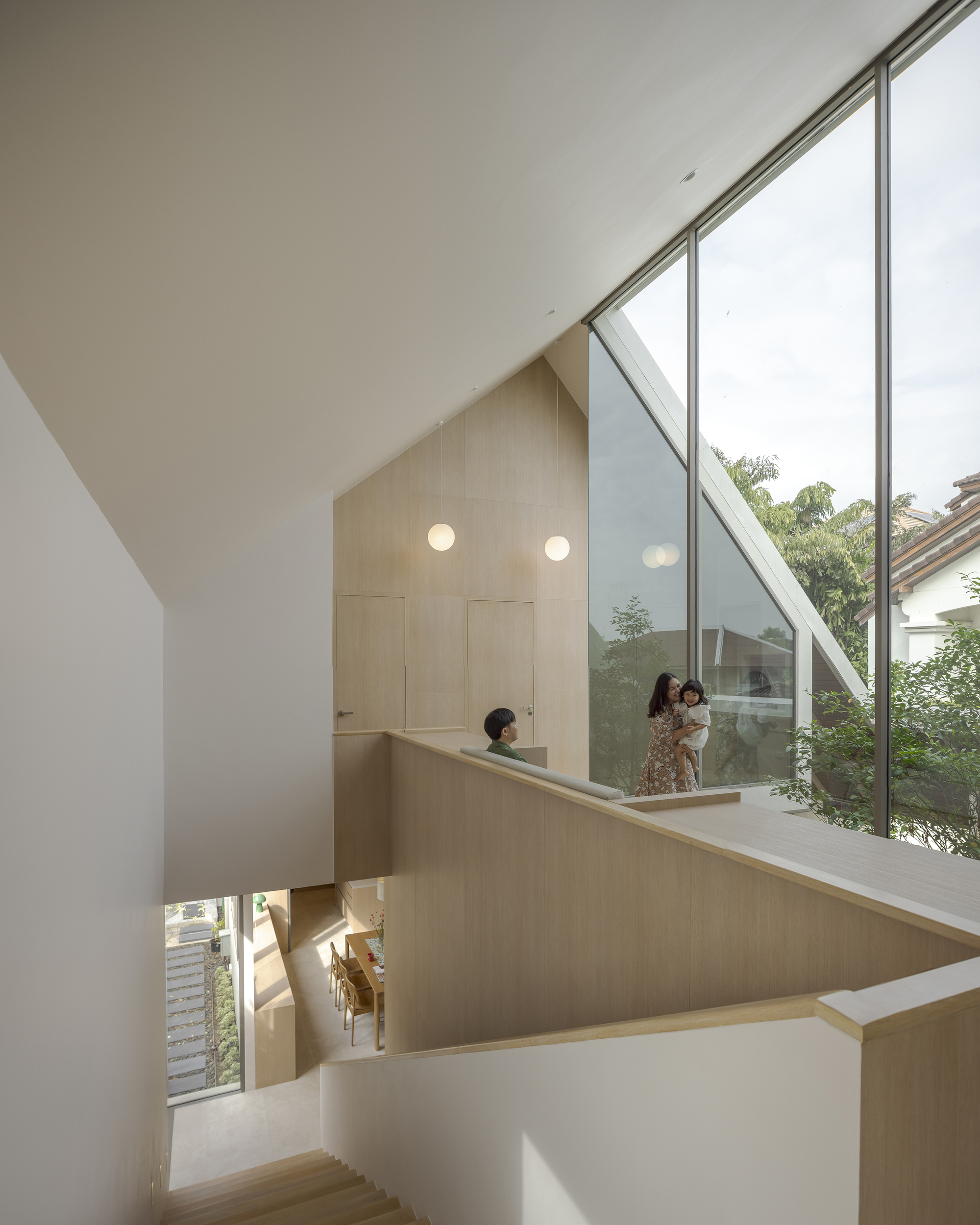 Double-height stairwell with sloped glazing and pale wood railings overlooking planted courtyard with occupants
