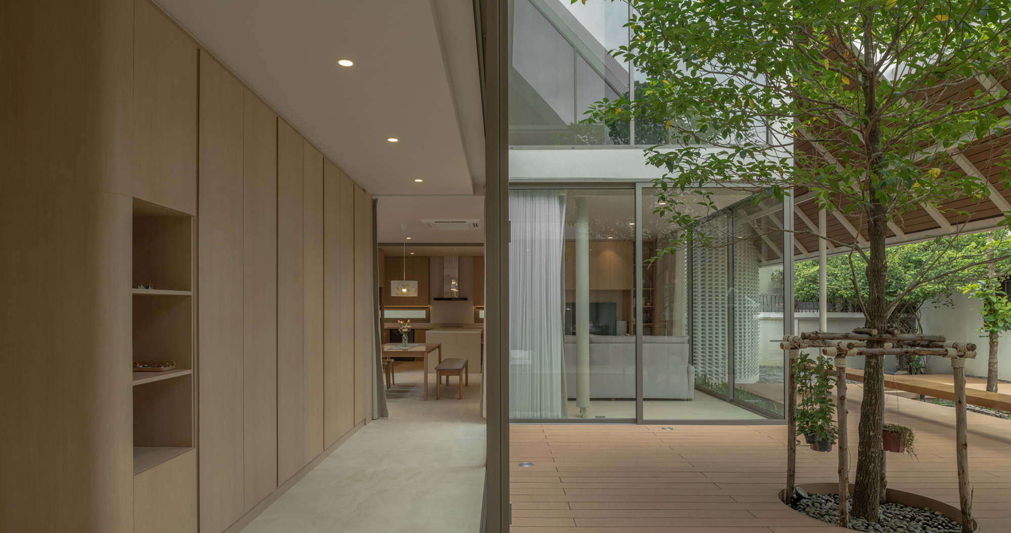 Interior courtyard with planted tree and glass walls connecting wood-paneled passages at dusk