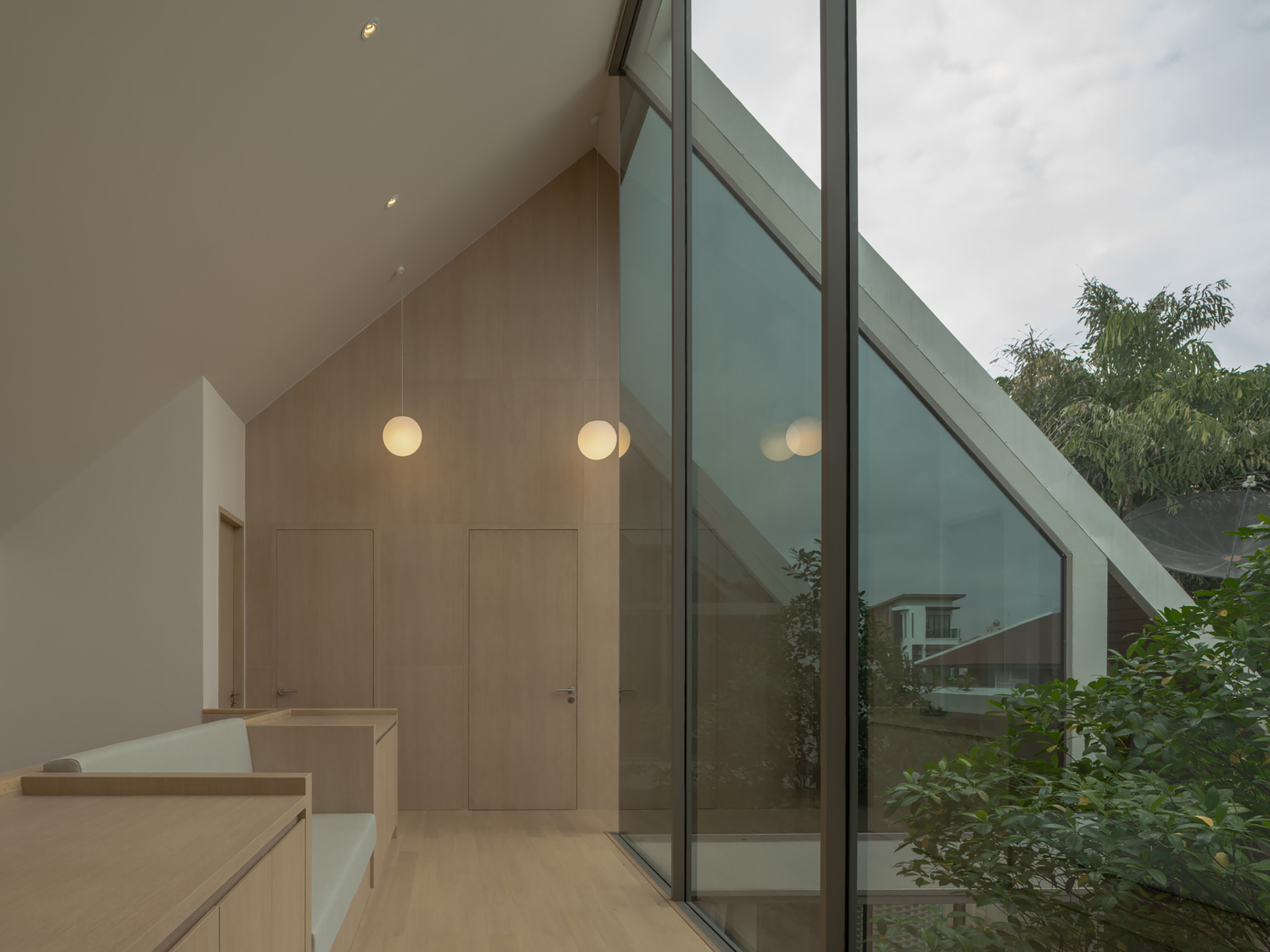 Interior hallway with sloped glazing, pendant lights, and pale wood cabinetry at dusk