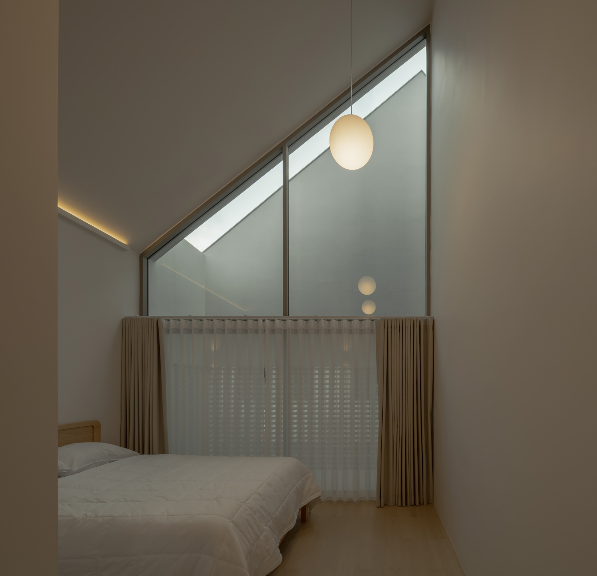 Bedroom with sloped skylight, sheer curtains, and illuminated pendant at twilight