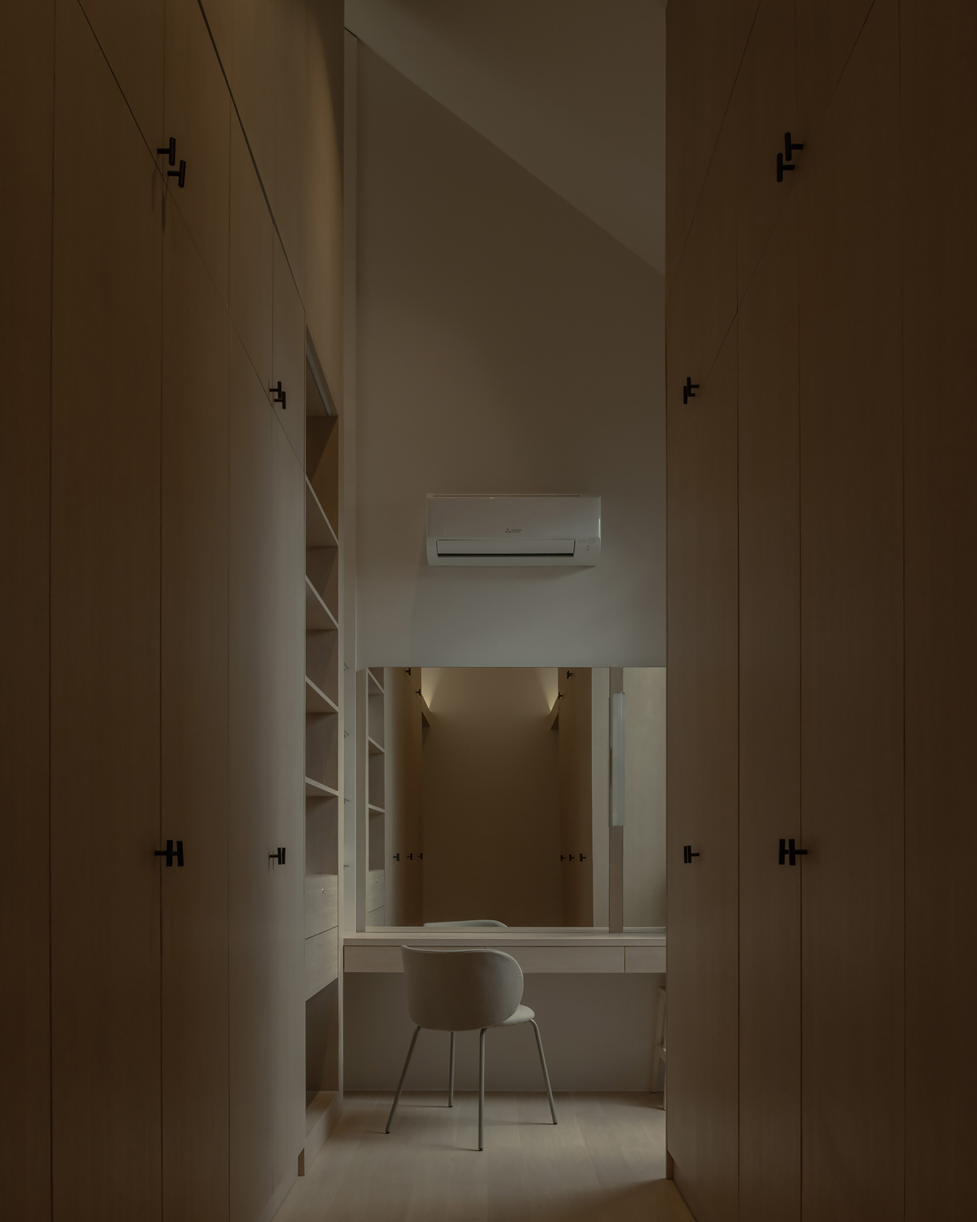 Narrow study alcove with built-in desk and shelving flanked by tall plywood storage cabinets in soft light