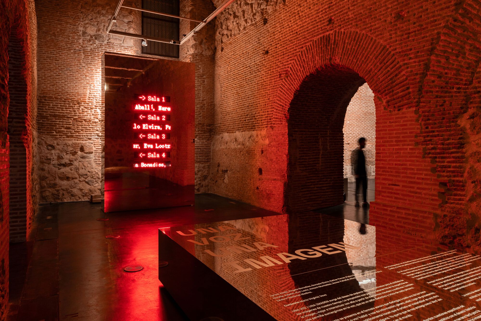 Brick archway framing a visitor standing in red light beside a reflective floor panel