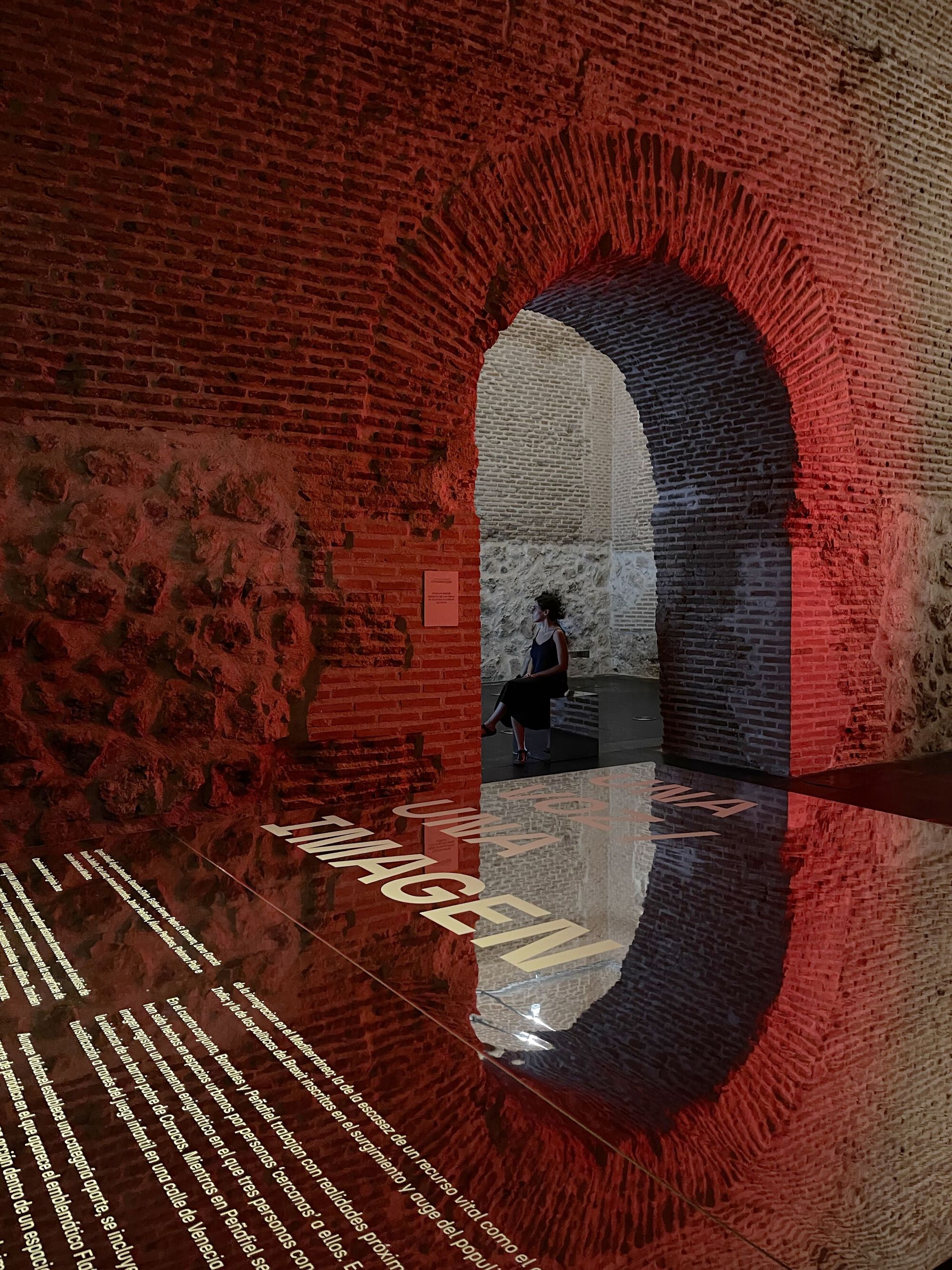 Brick vault reflected in a red acrylic floor panel with a visitor visible through the arch