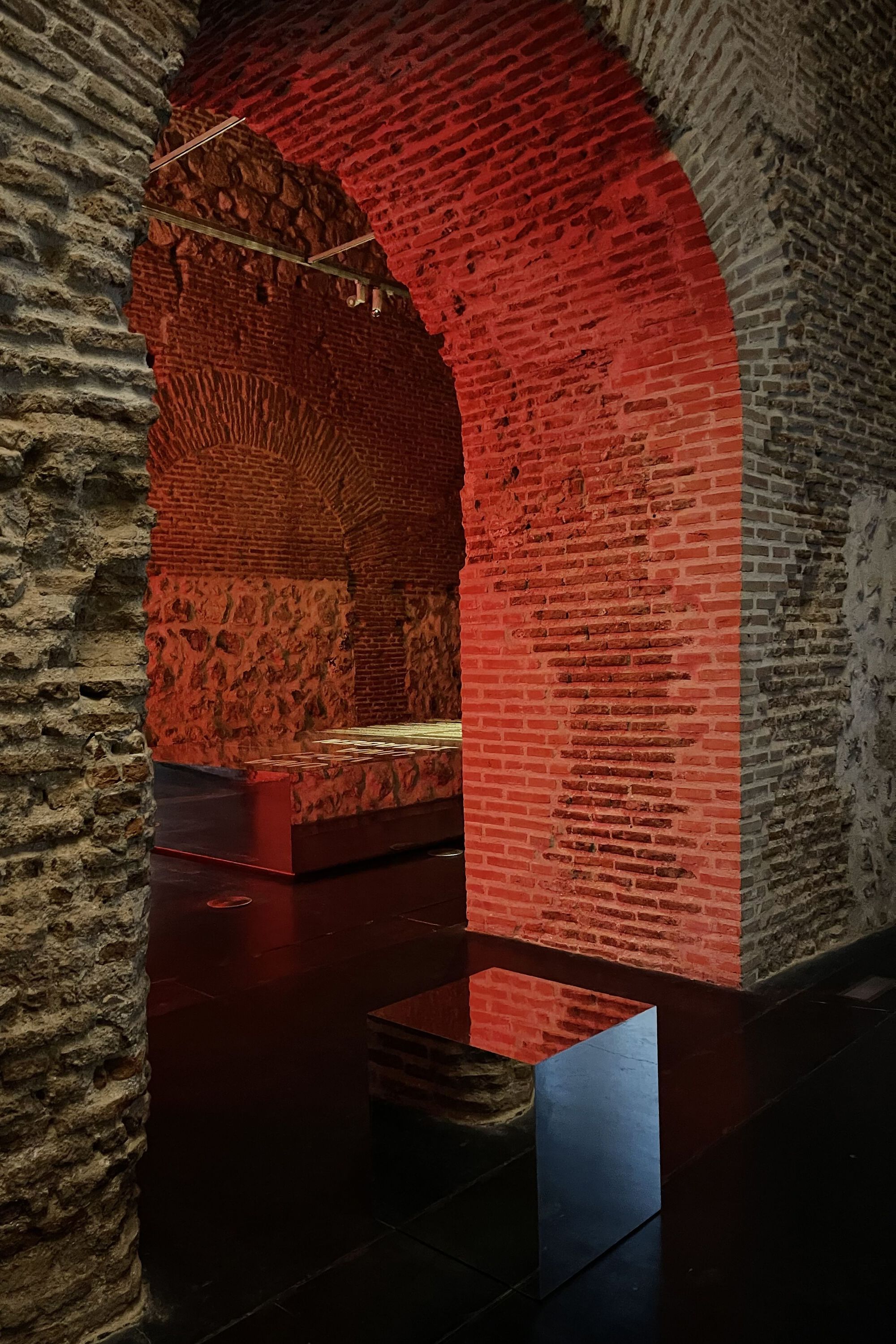 Close-up of a brick arch transitioning from red light to shadow above a reflective floor