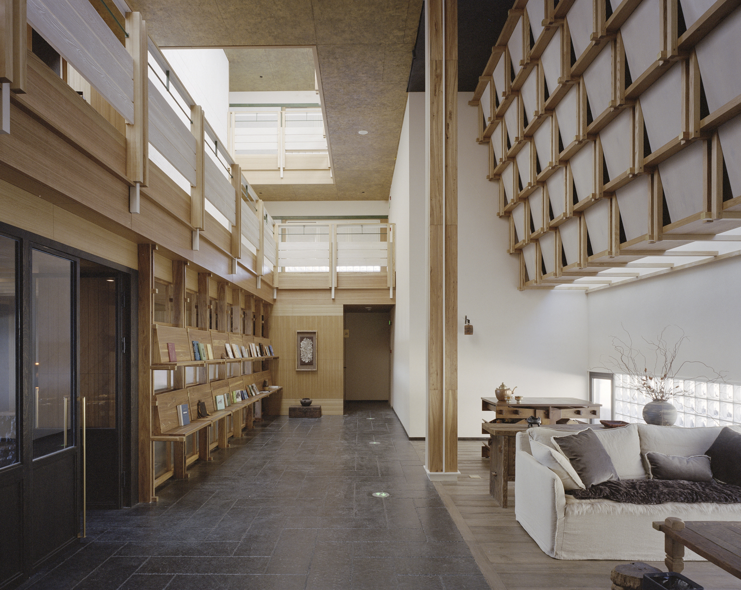 Double-height lobby with timber shelving, exposed wooden columns, and skylights above a seating area