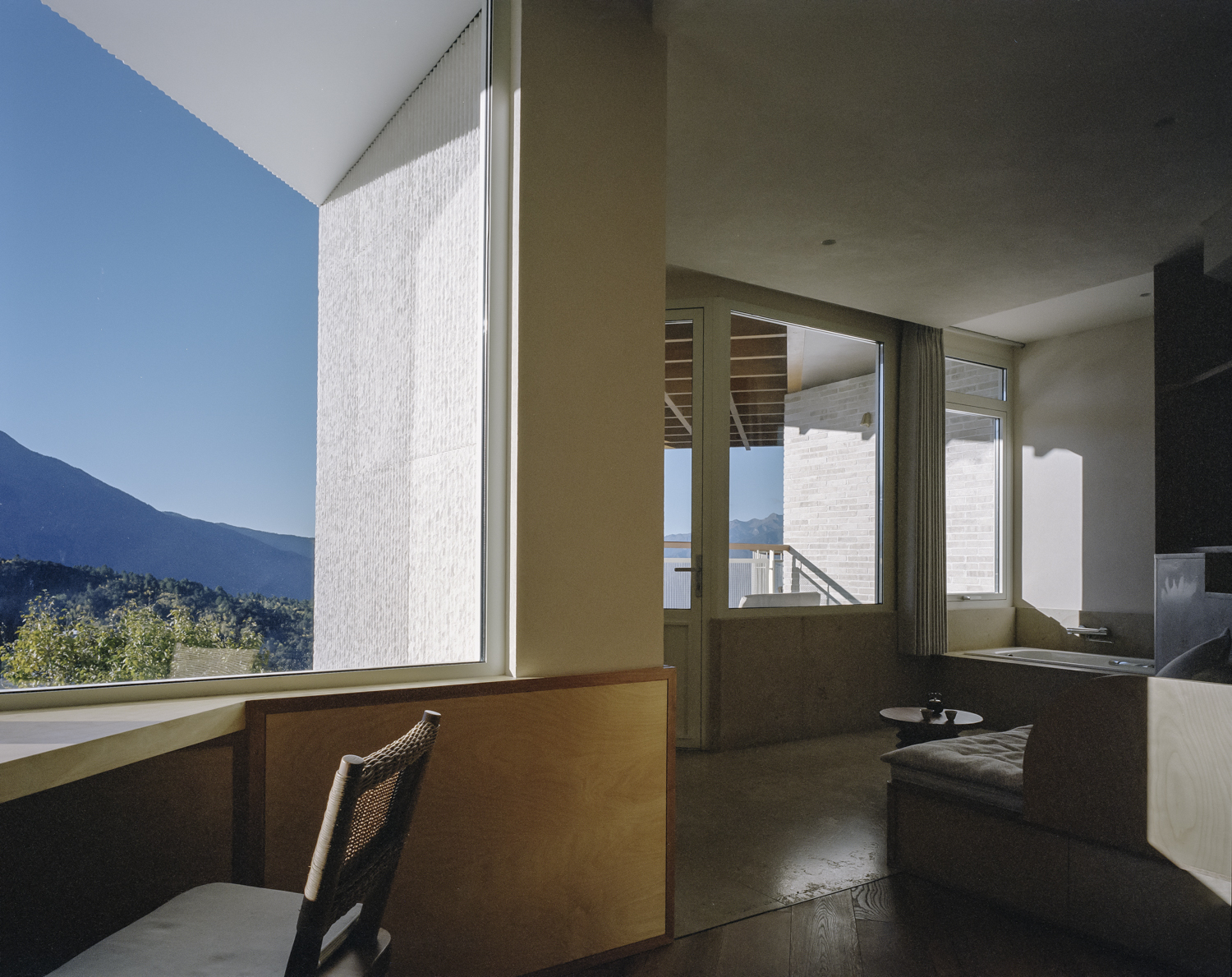 Interior corner desk overlooking mountain landscape through floor-to-ceiling glass under clear blue sky