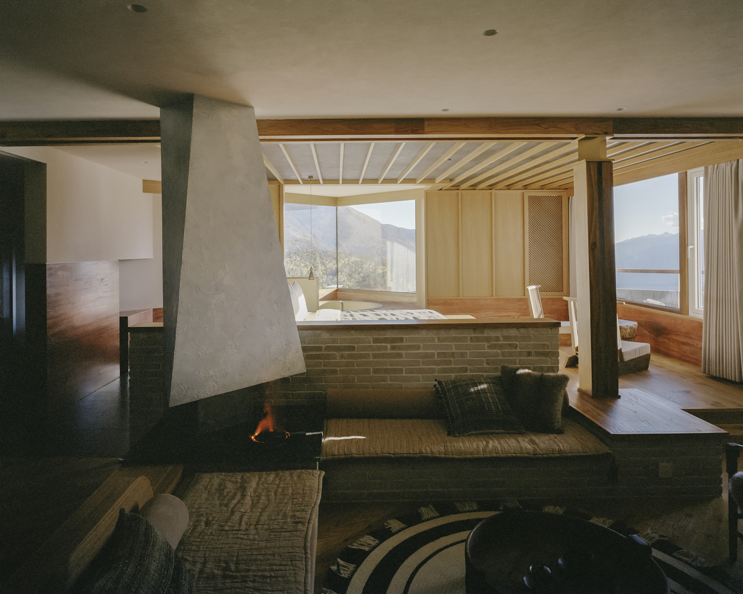 Sunken living area with concrete fireplace and timber-slatted ceiling framing mountain views