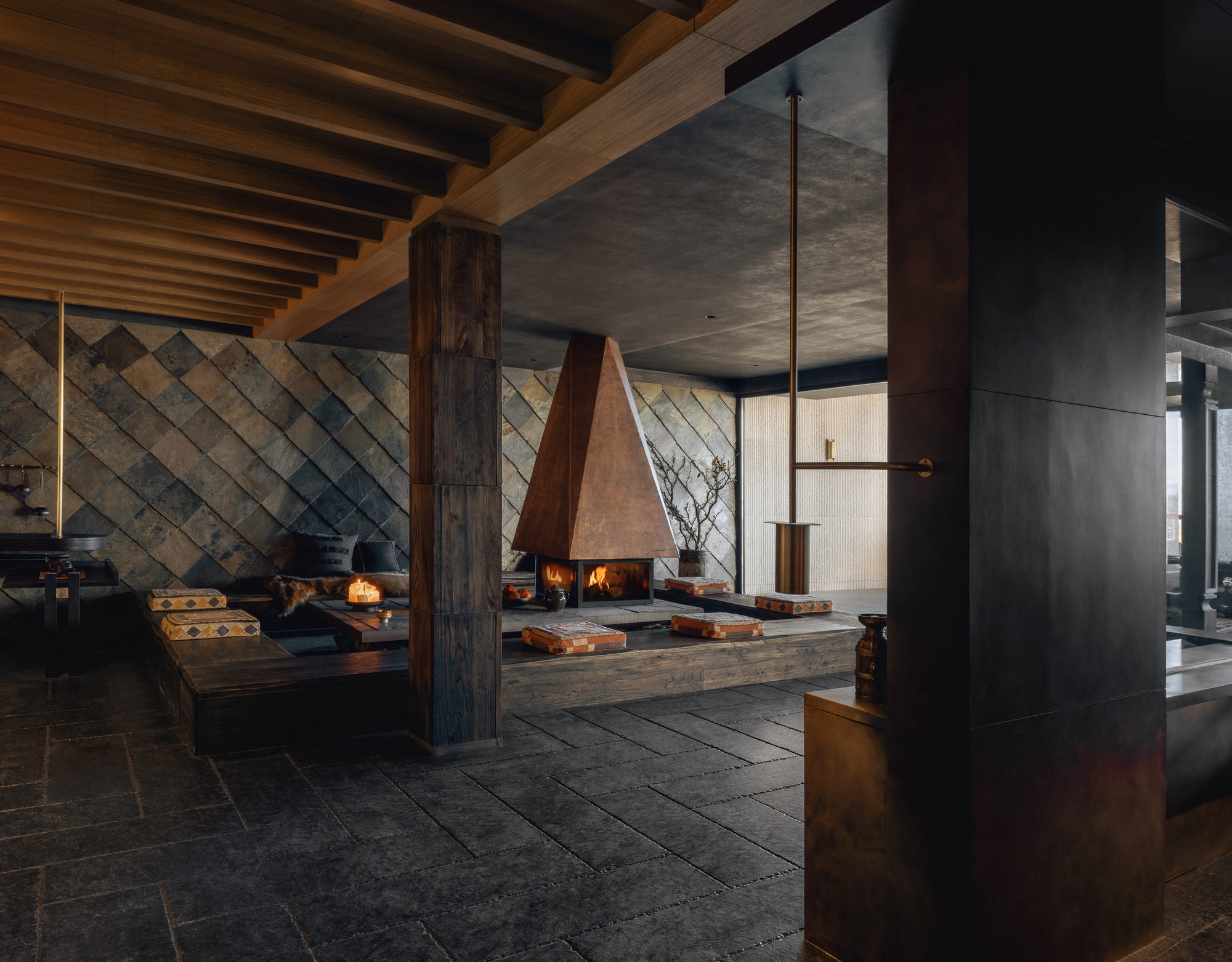 Pyramidal copper fireplace suspended over sunken seating platform with diamond-patterned wall behind