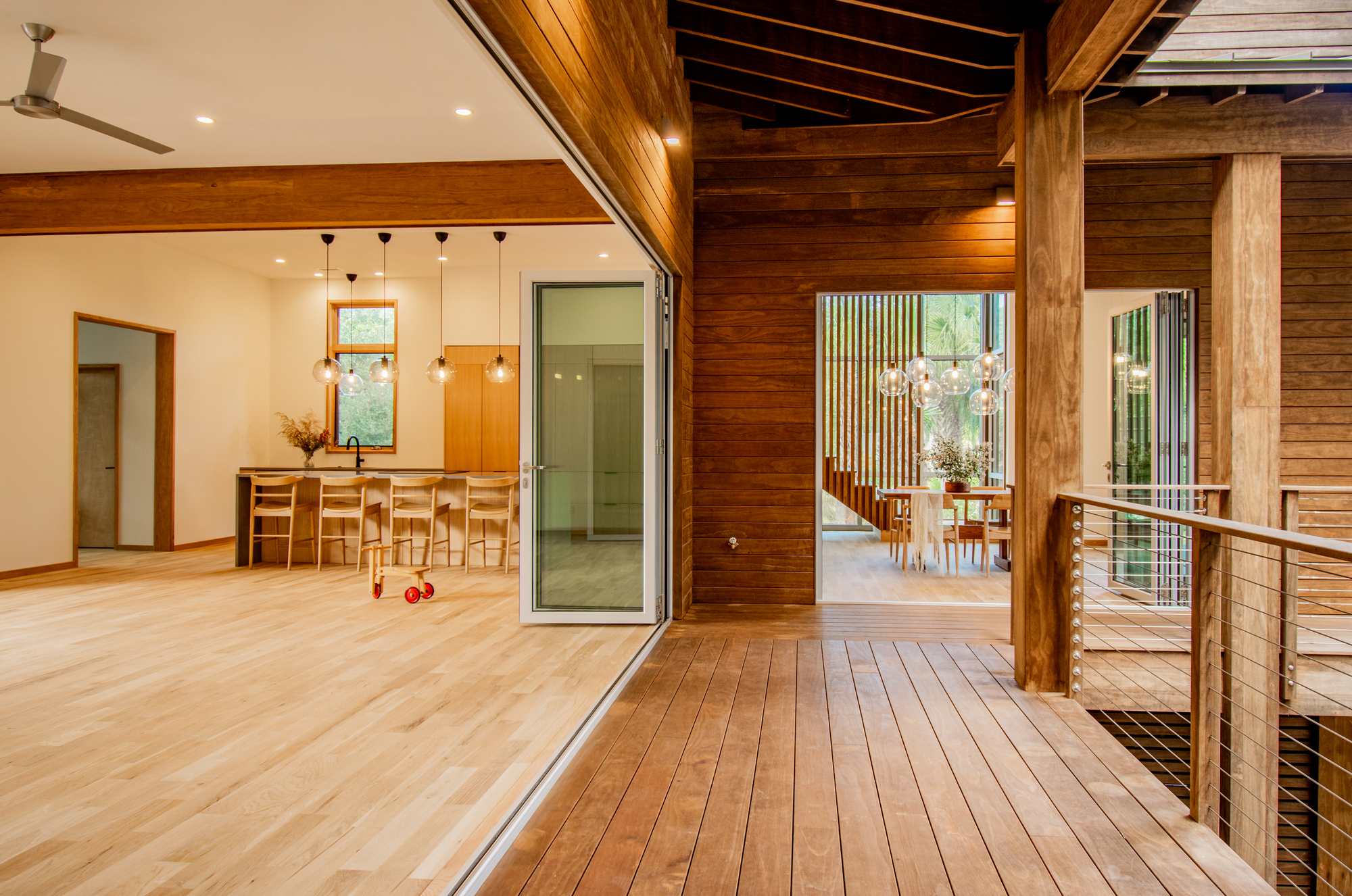 Open-plan living space with exposed wood ceiling beams and horizontal plank walls opening to deck