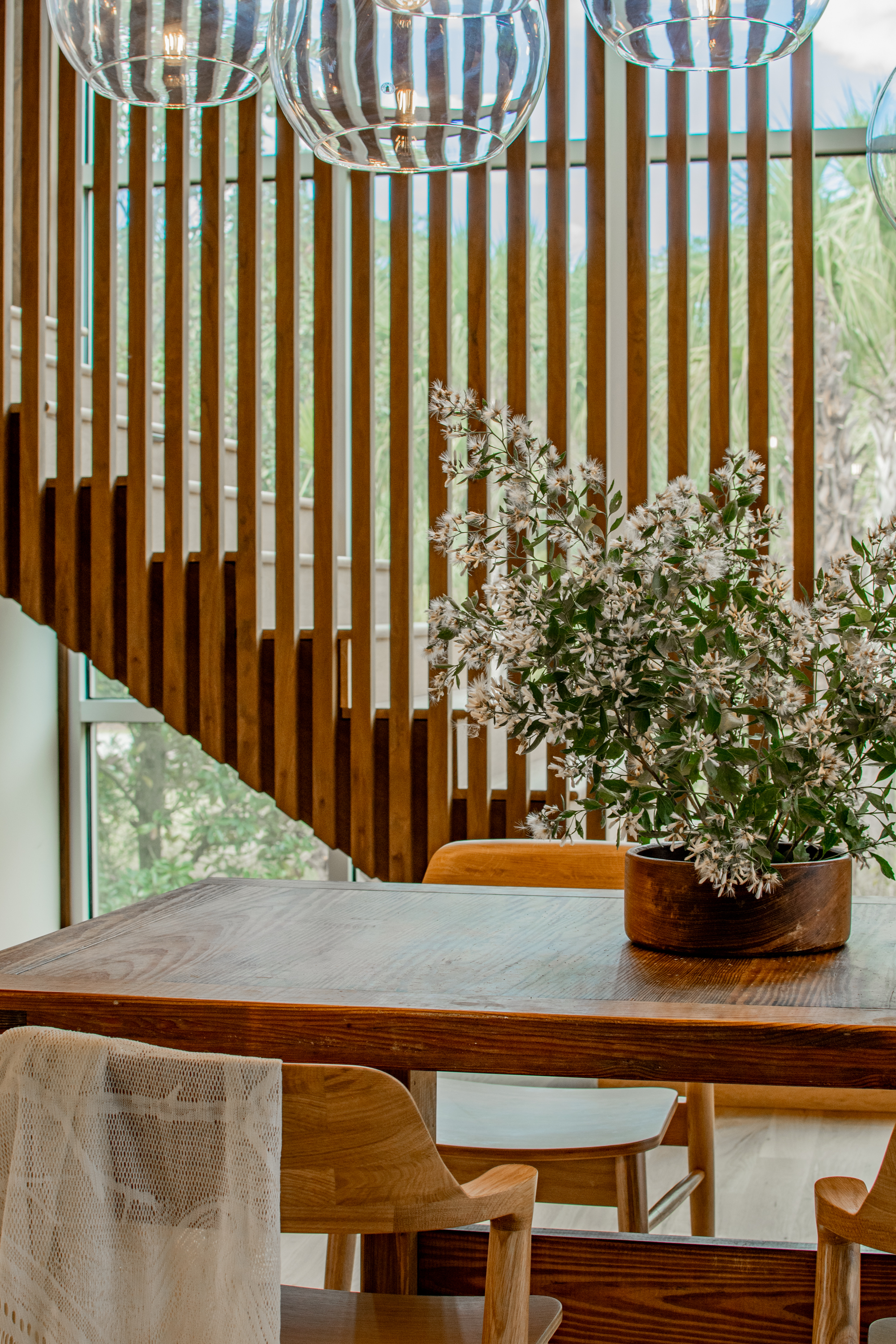Dining table with clear glass pendant lights and flowering branches against vertical timber batten wall