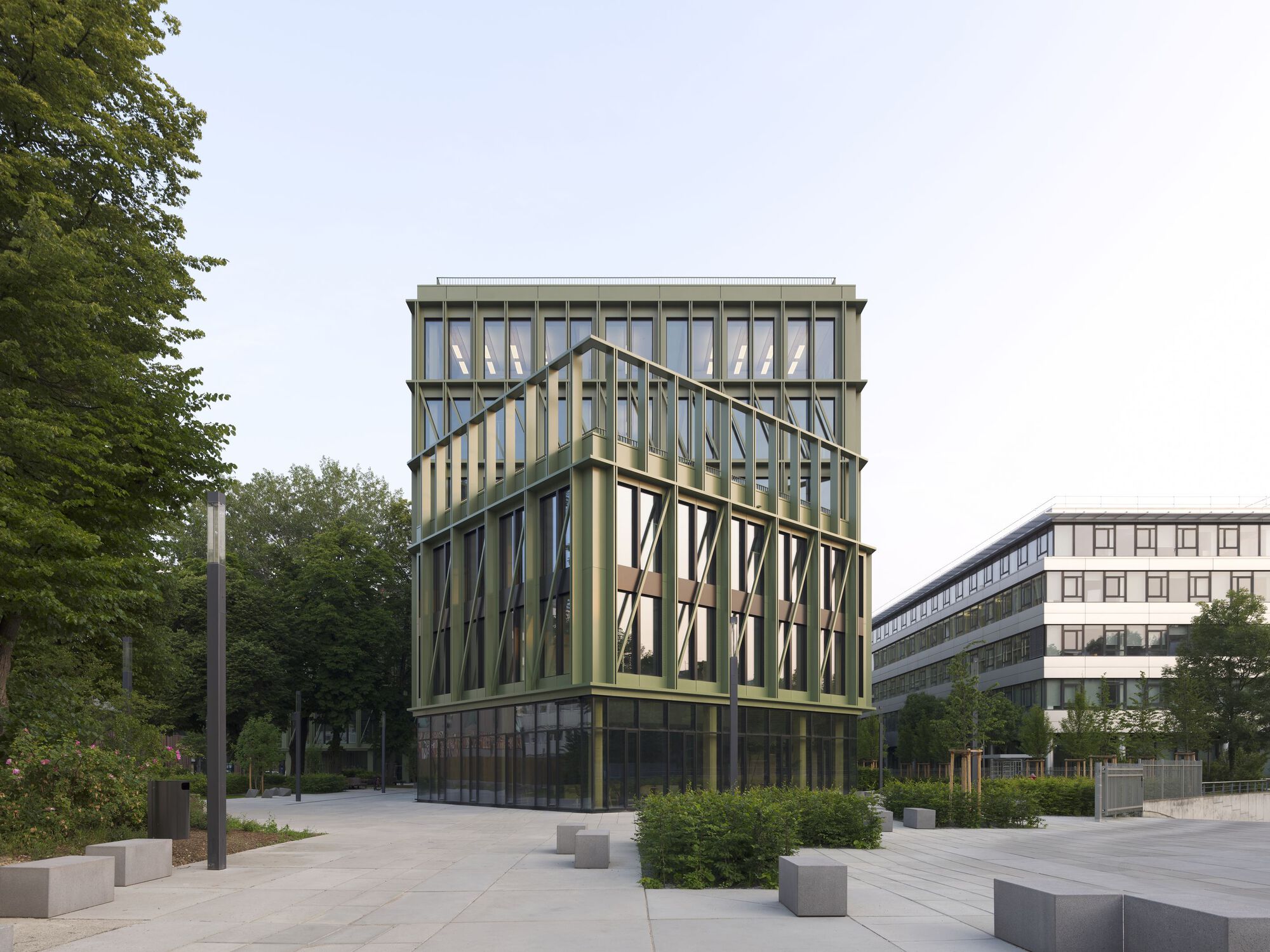 Green metal-framed facade with diagonal bracing visible through glazing in an overcast plaza setting
