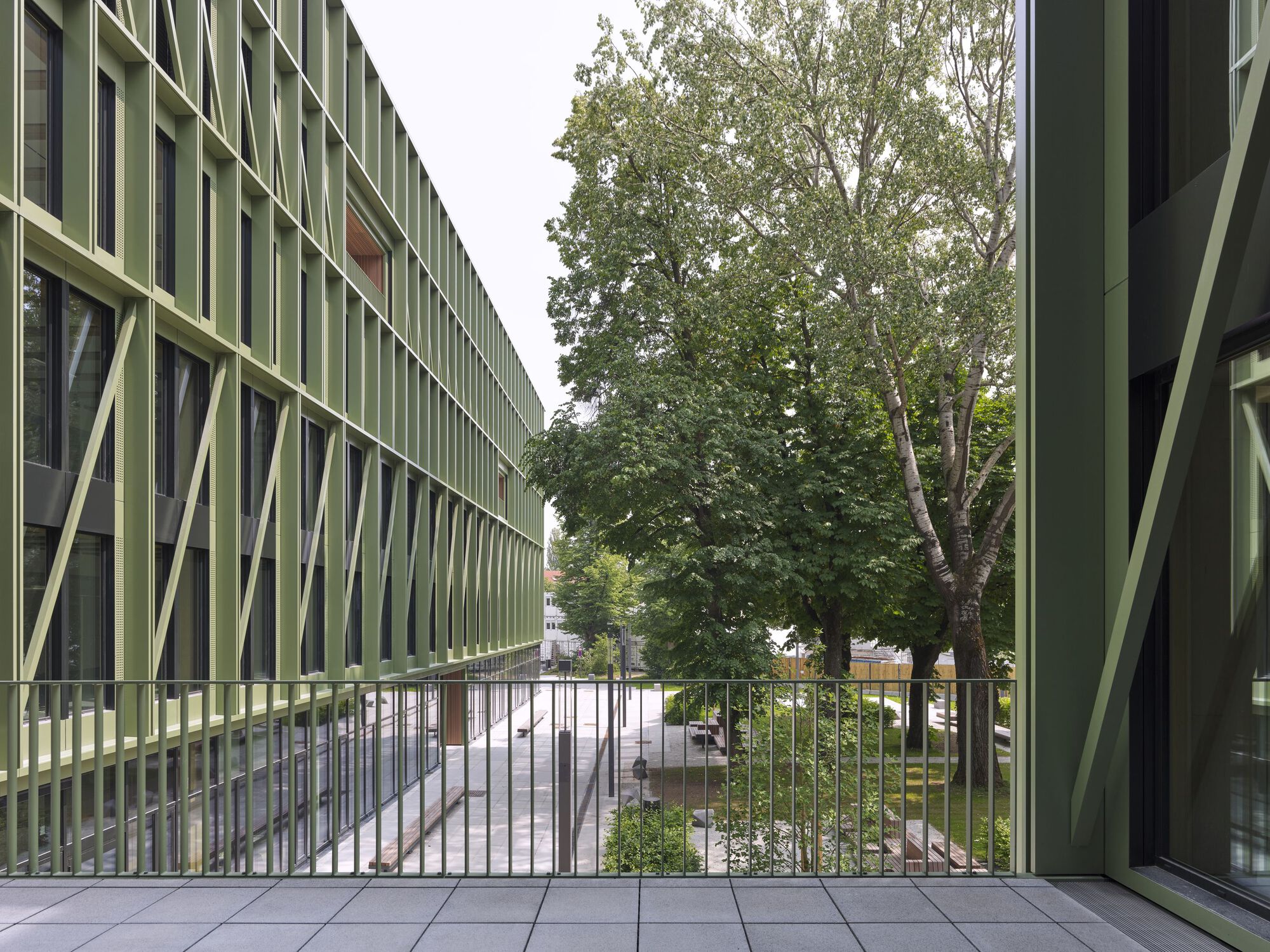 Exterior balcony with metal railing overlooking a tree-lined courtyard and paved street below